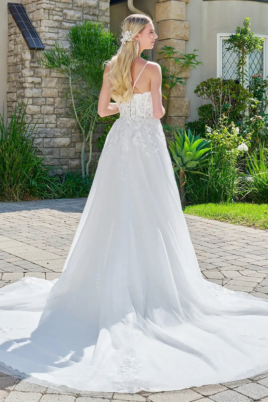 Woman in a white wedding dress standing outdoors with a stone building and greenery in the background