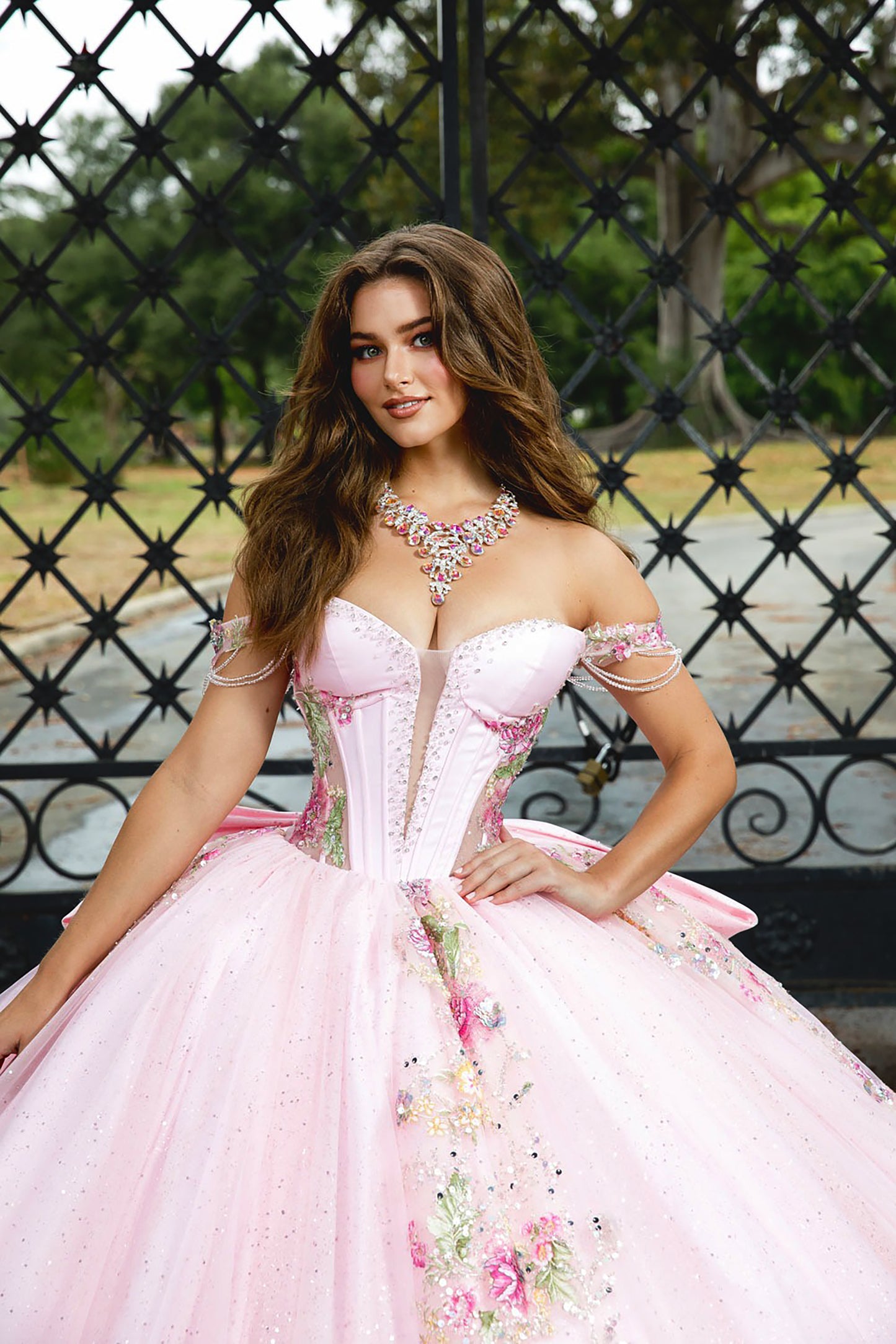 Woman in a pink formal gown with floral details sitting outdoors.