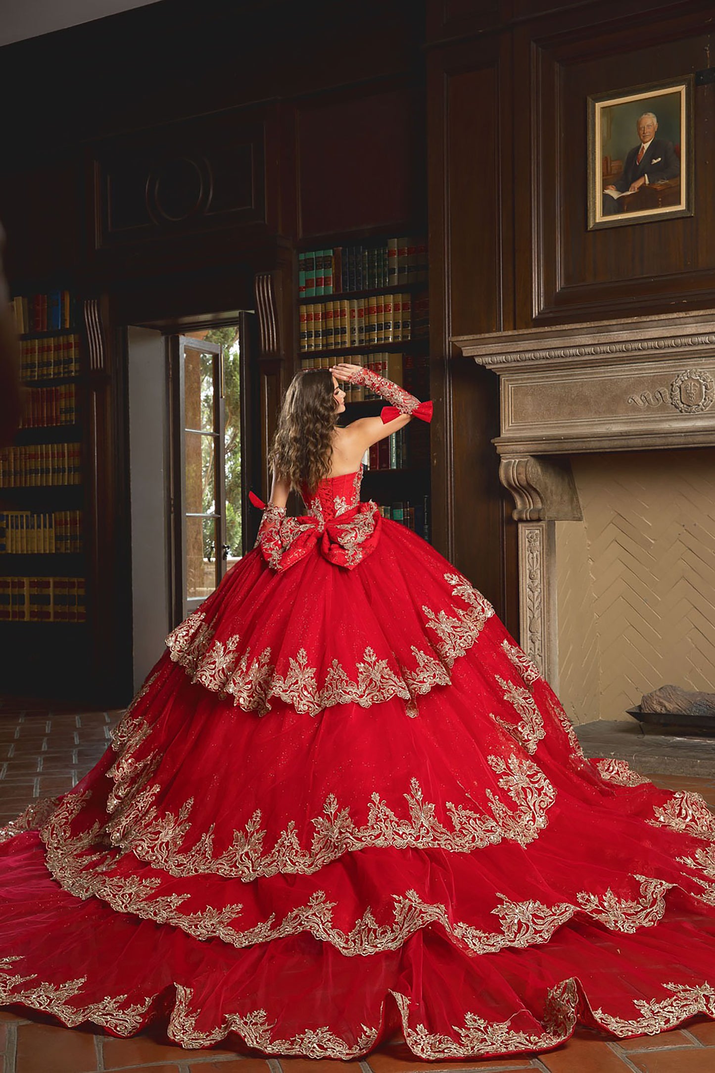 Woman in a red and gold formal gown standing in a room with bookshelves and a fireplace.