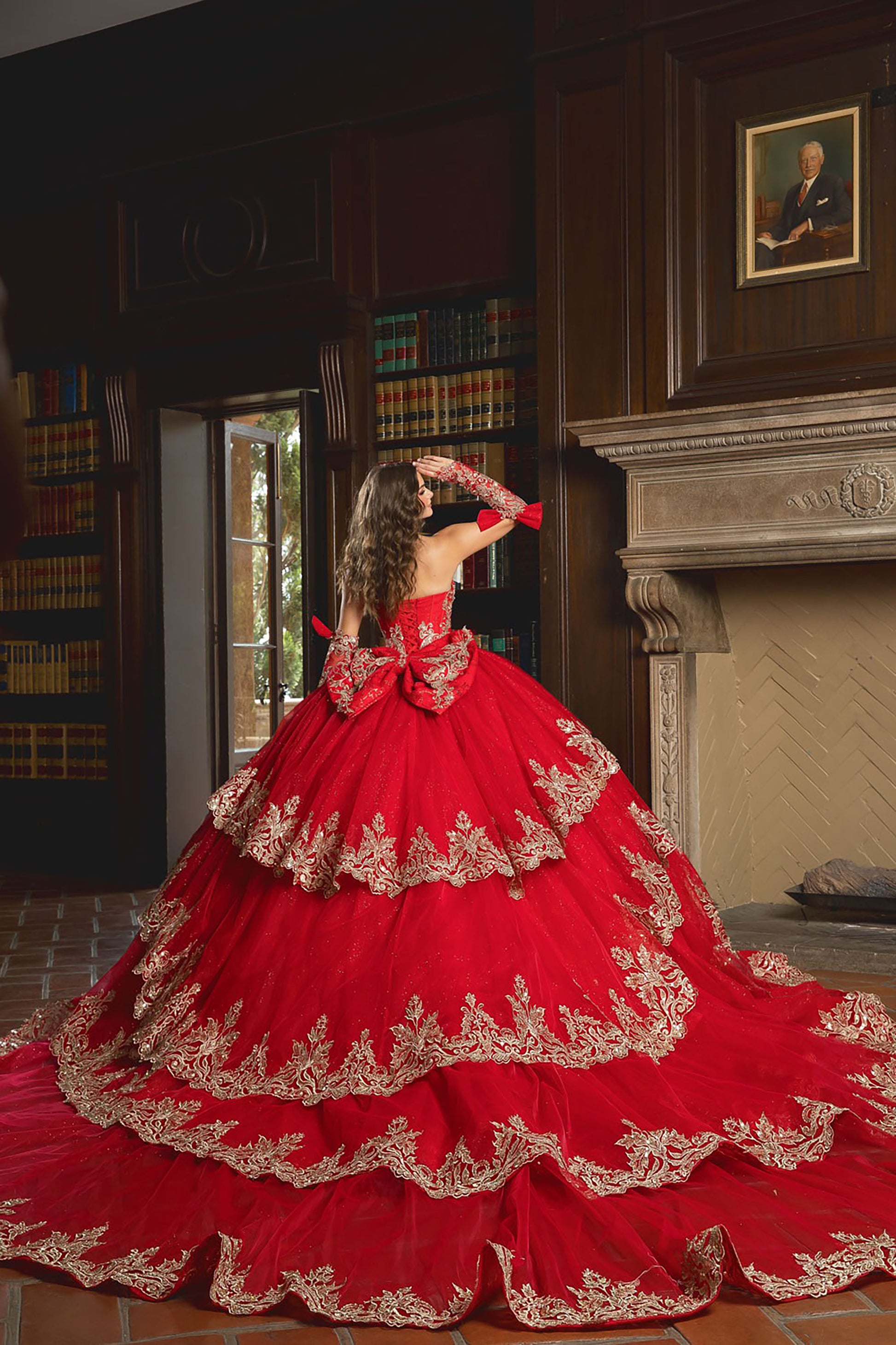 Woman in a red and gold formal gown standing in a room with bookshelves and a fireplace.