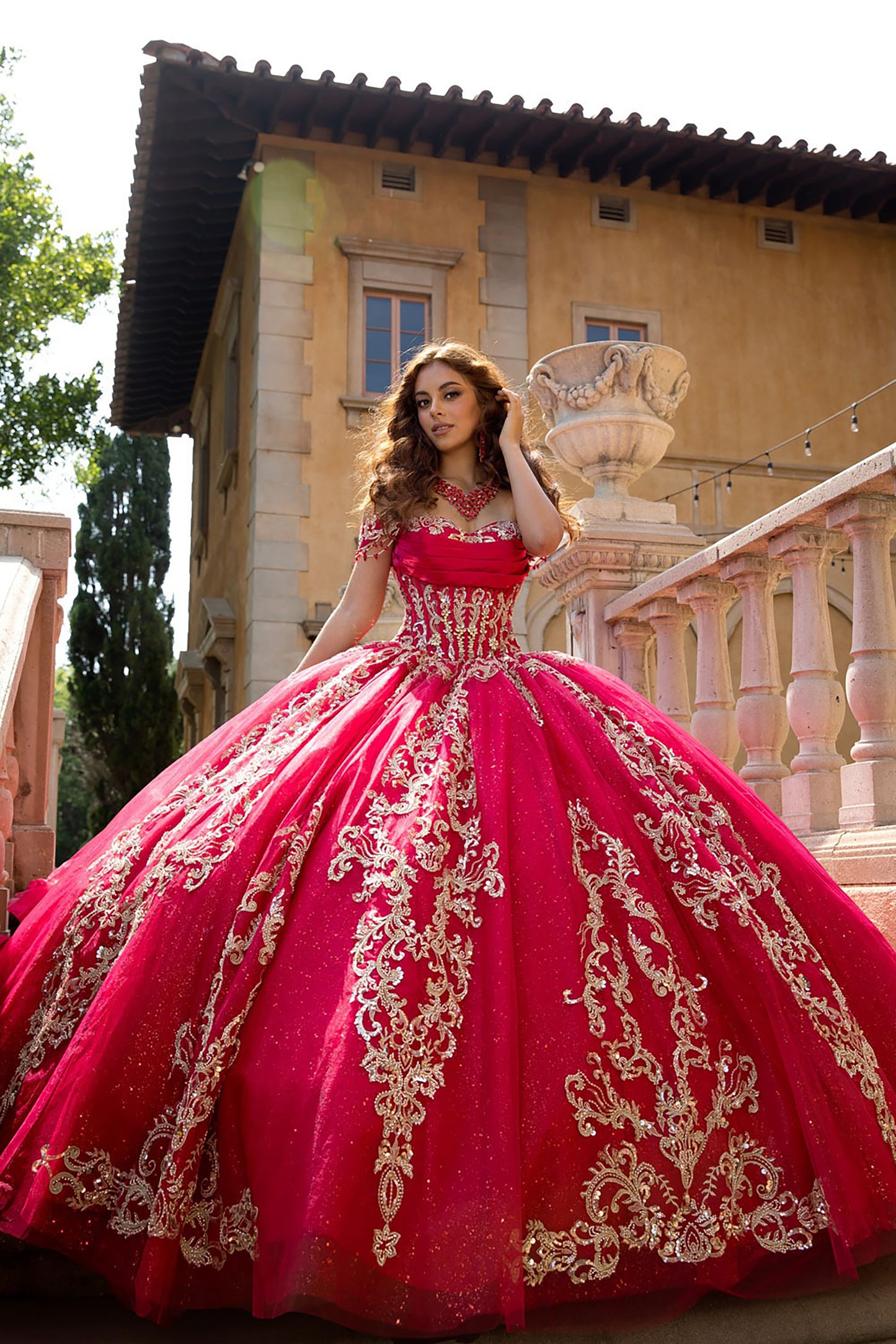 Woman in a red and gold ball gown standing in front of a building with classical architecture.