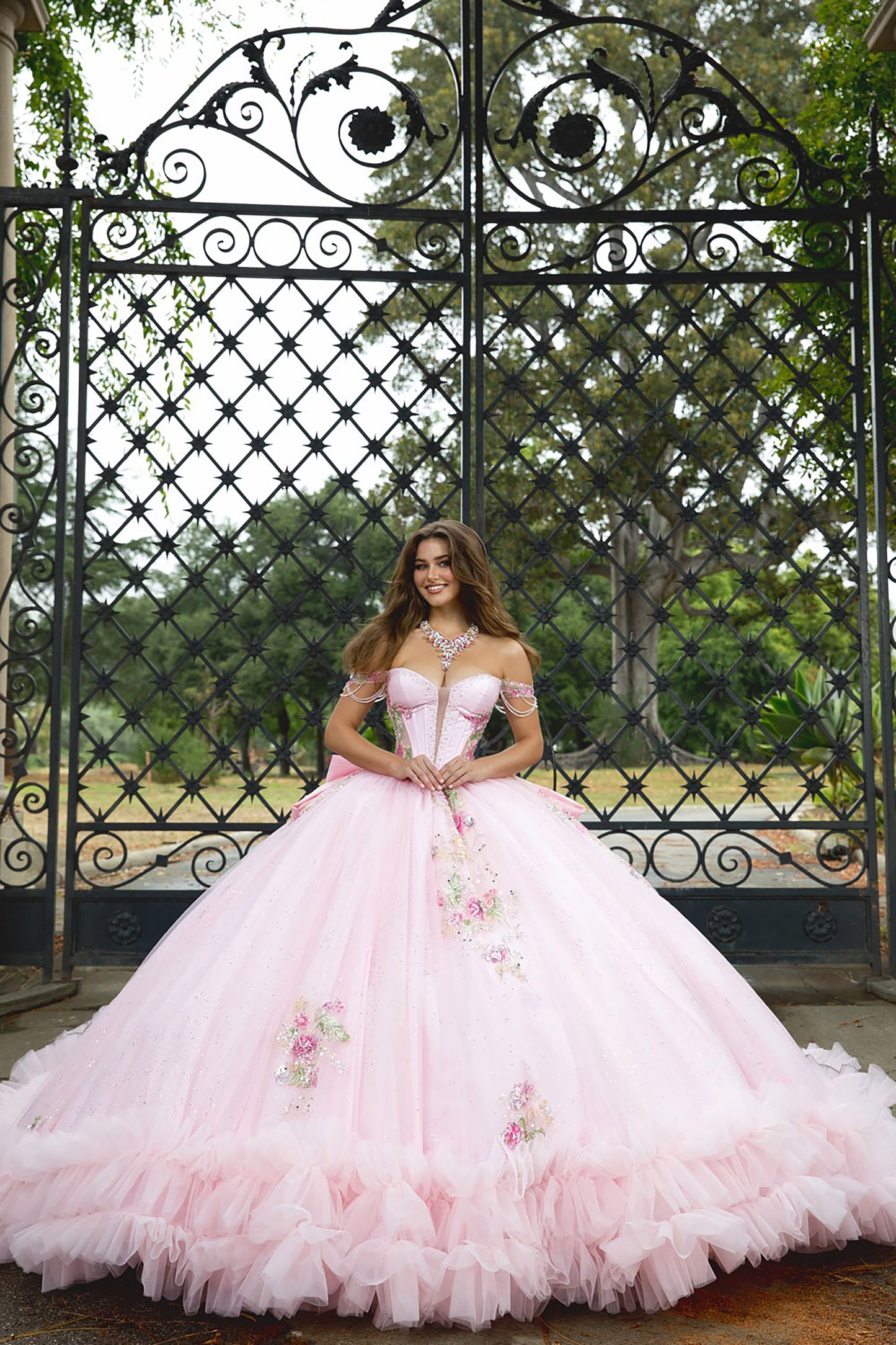 Woman in a pink ball gown standing in front of an ornate metal gate.