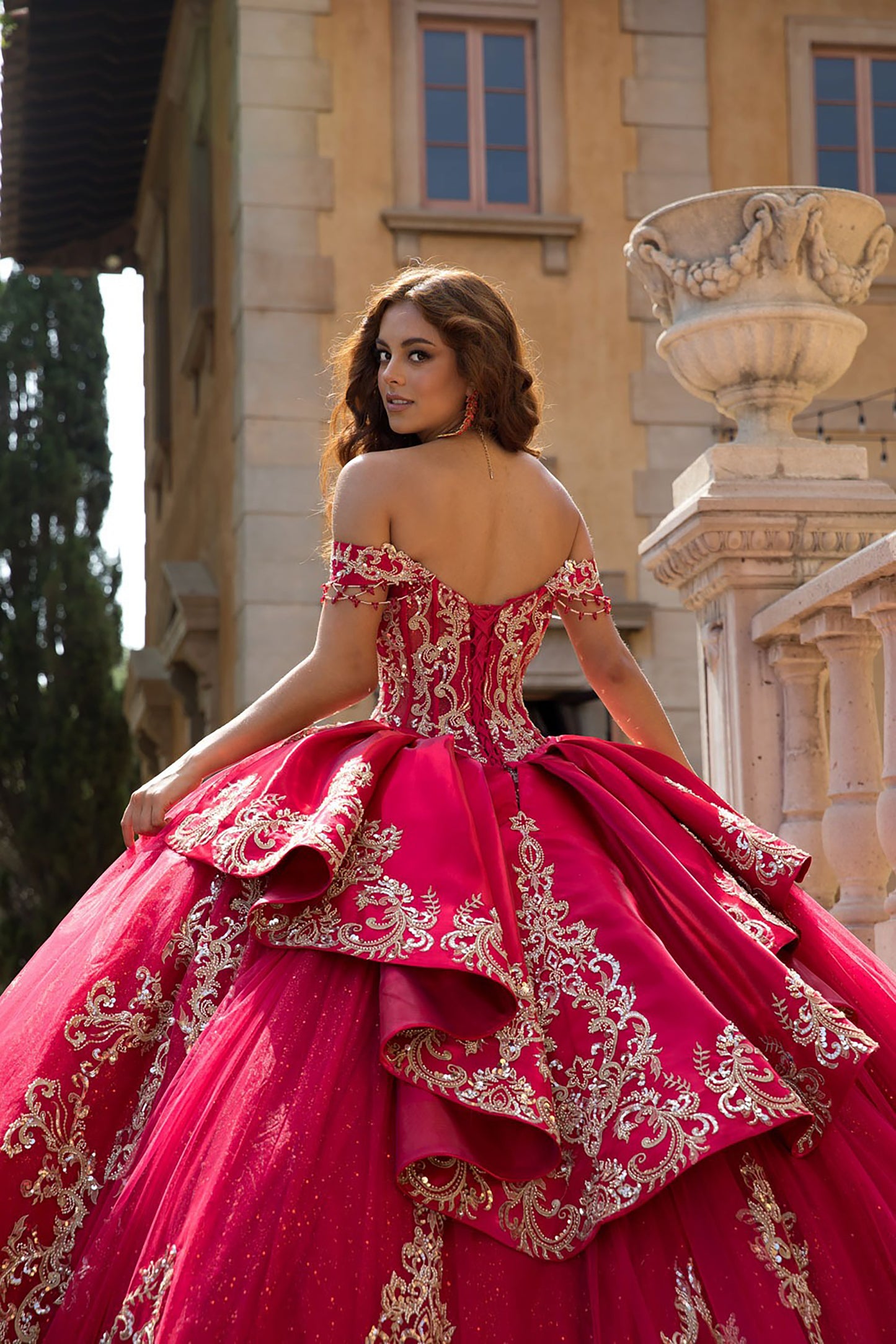 Woman in a red and gold gown standing outdoors with classical architecture in the background