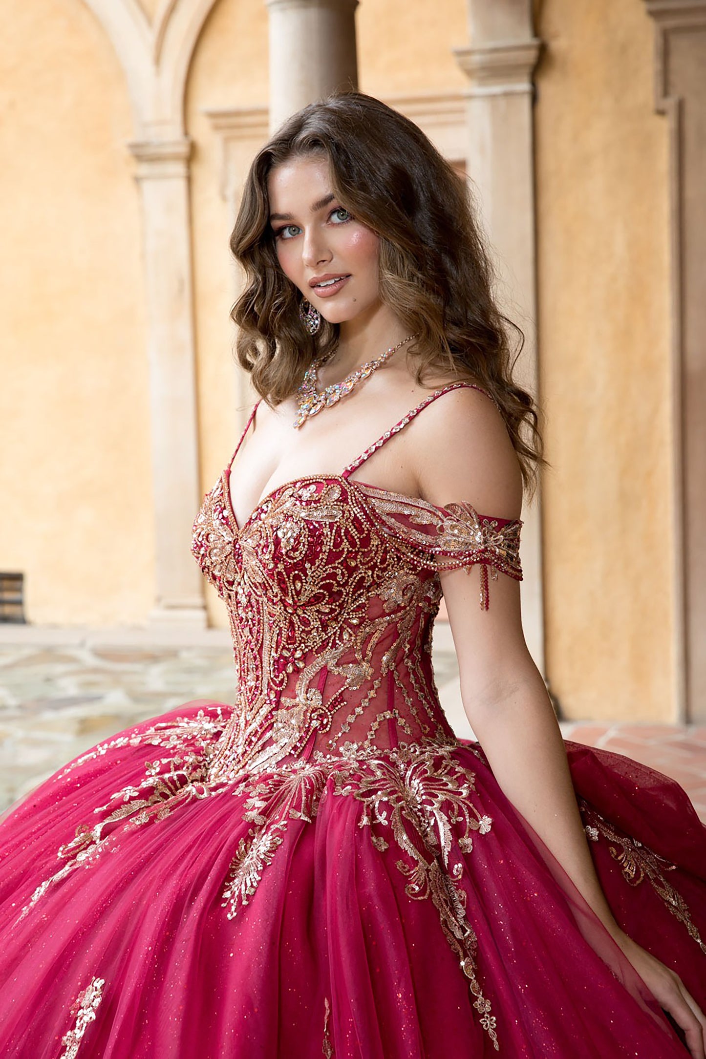 Woman in a red and gold formal gown standing in an outdoor setting with columns.
