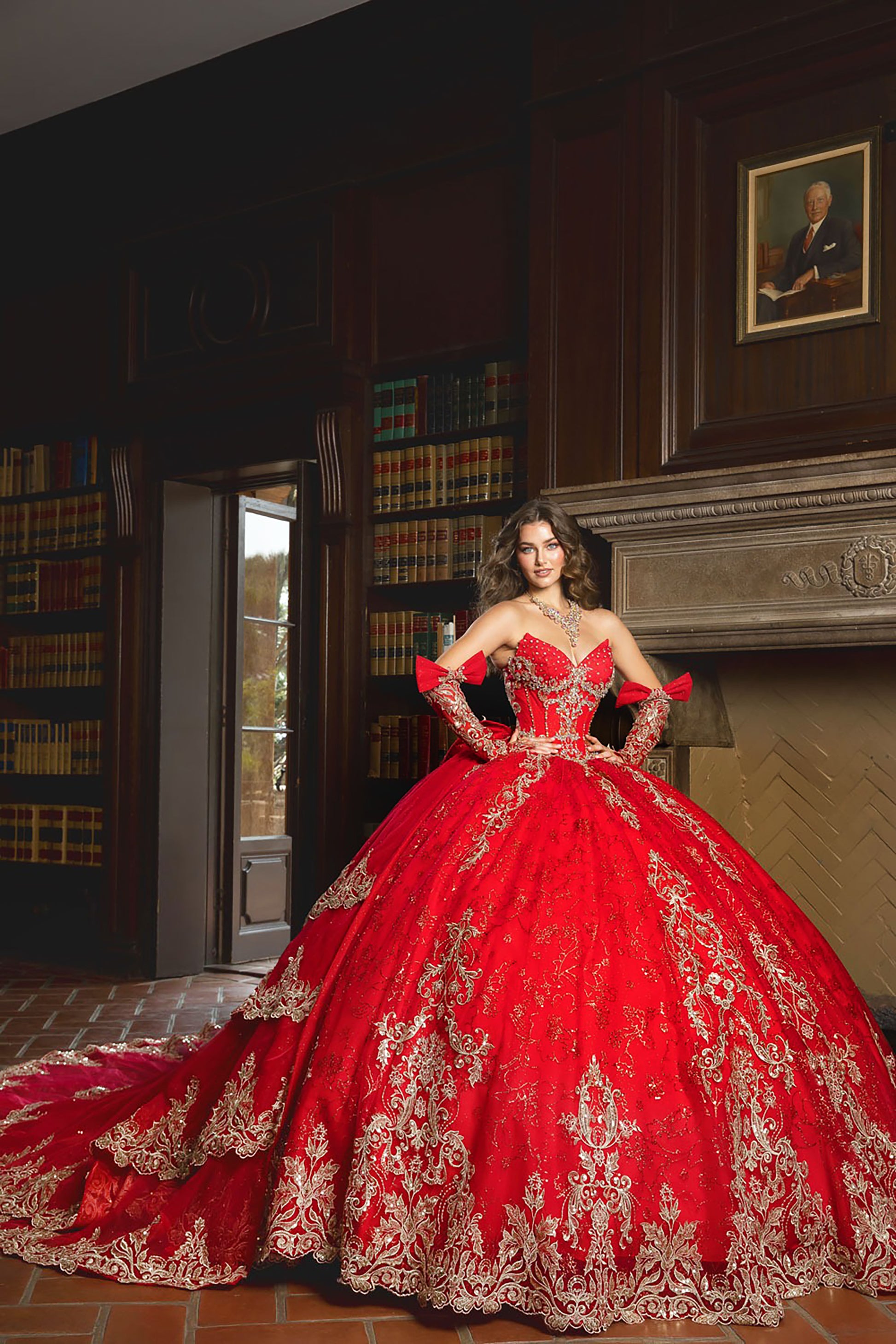 Woman in a red and gold embroidered gown standing in a room with bookshelves and a fireplace.