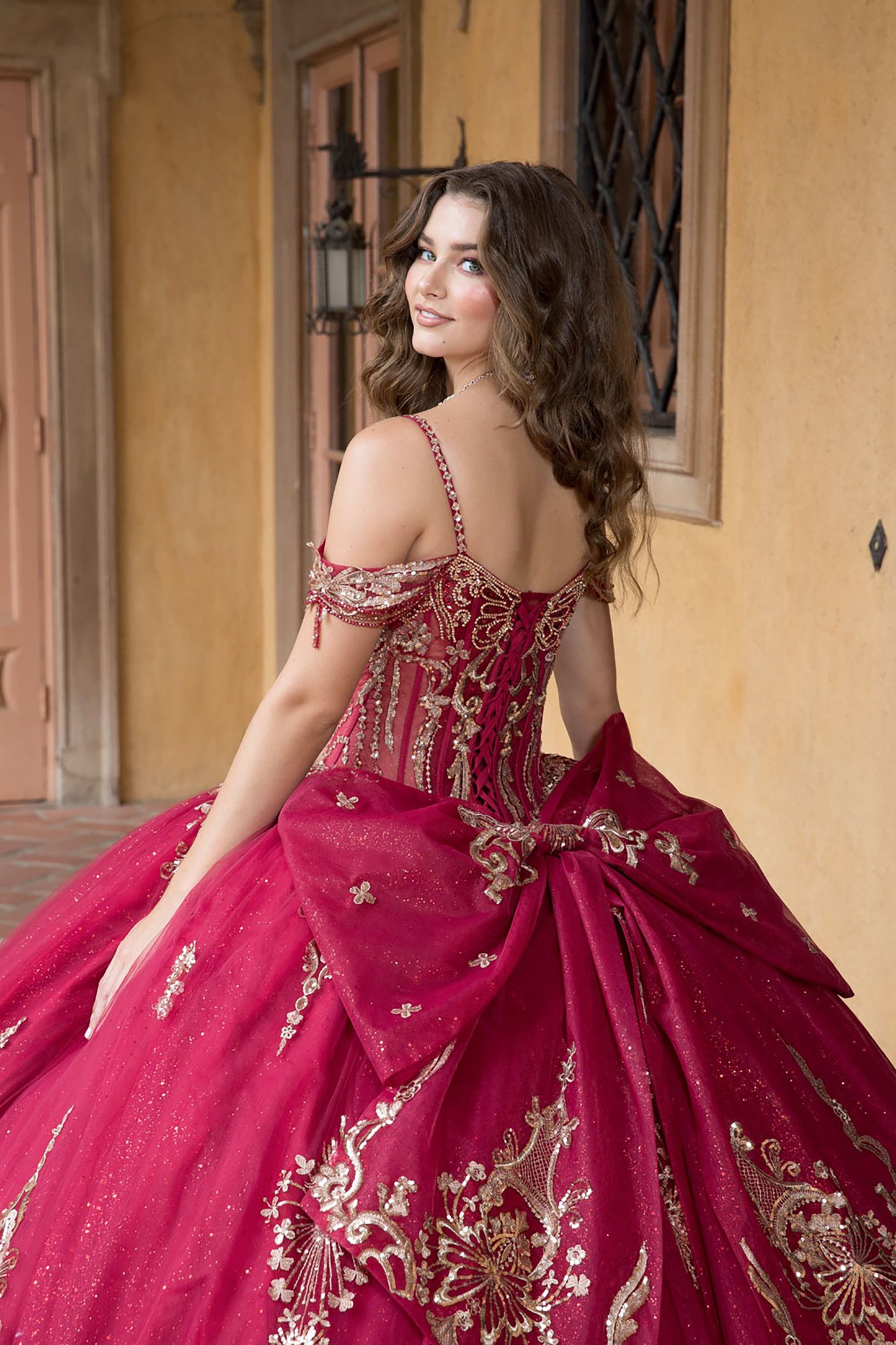 Woman in a red and gold embroidered dress standing in front of a building entrance.
