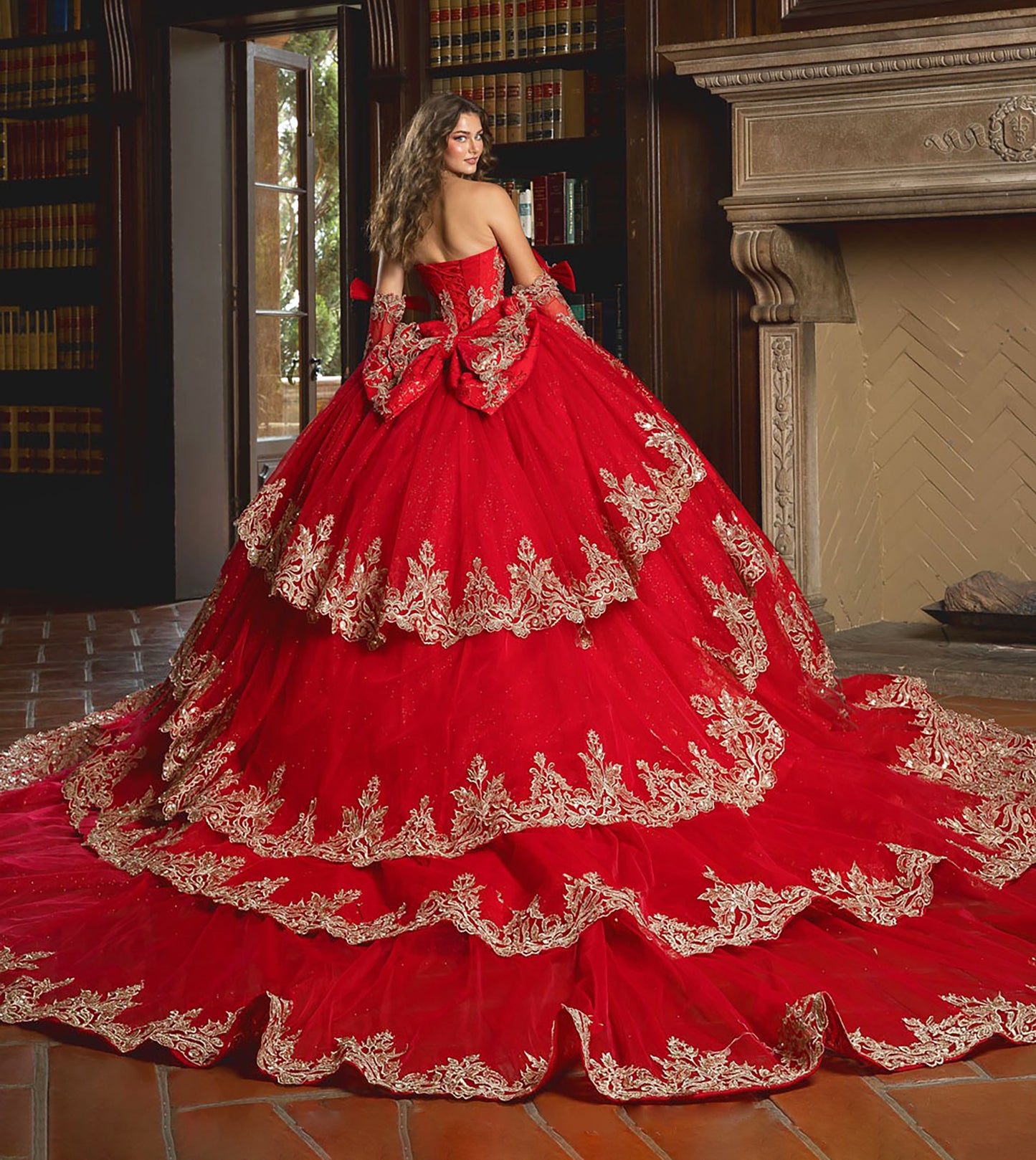 Red ball gown with gold embroidery in a room with books and a fireplace.