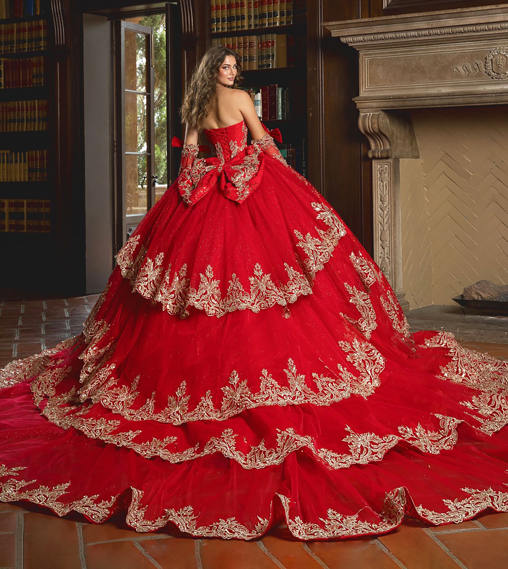 Red ball gown with gold embroidery in a room with books and a fireplace.