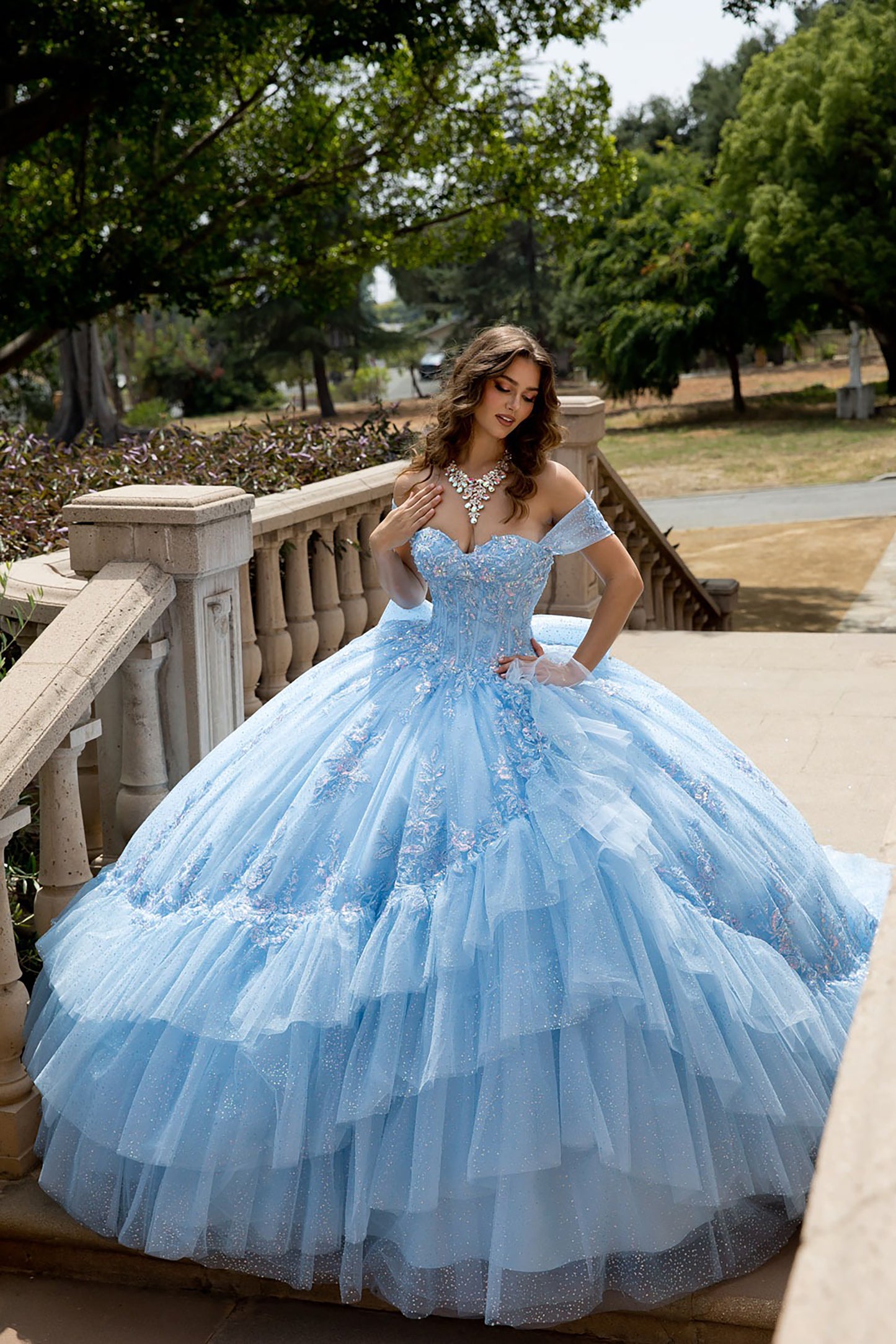 Woman in a light blue ball gown standing outdoors on a stone staircase.