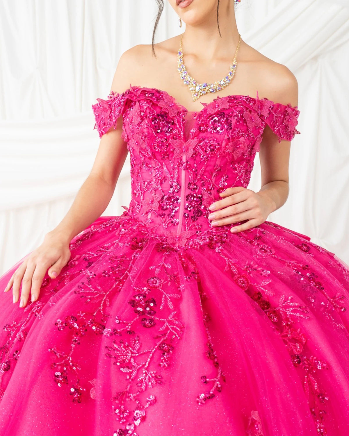 Close-up view reveals fuchsia quinceanera dress with off-shoulder neckline, floral embroidery, butterfly appliques, and sequin details.