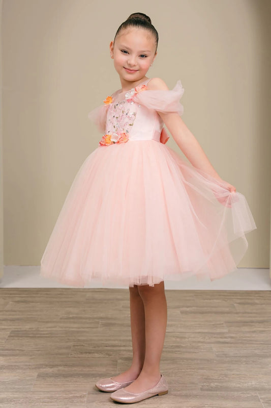 Young girl in a pink dress with floral details standing against a plain background