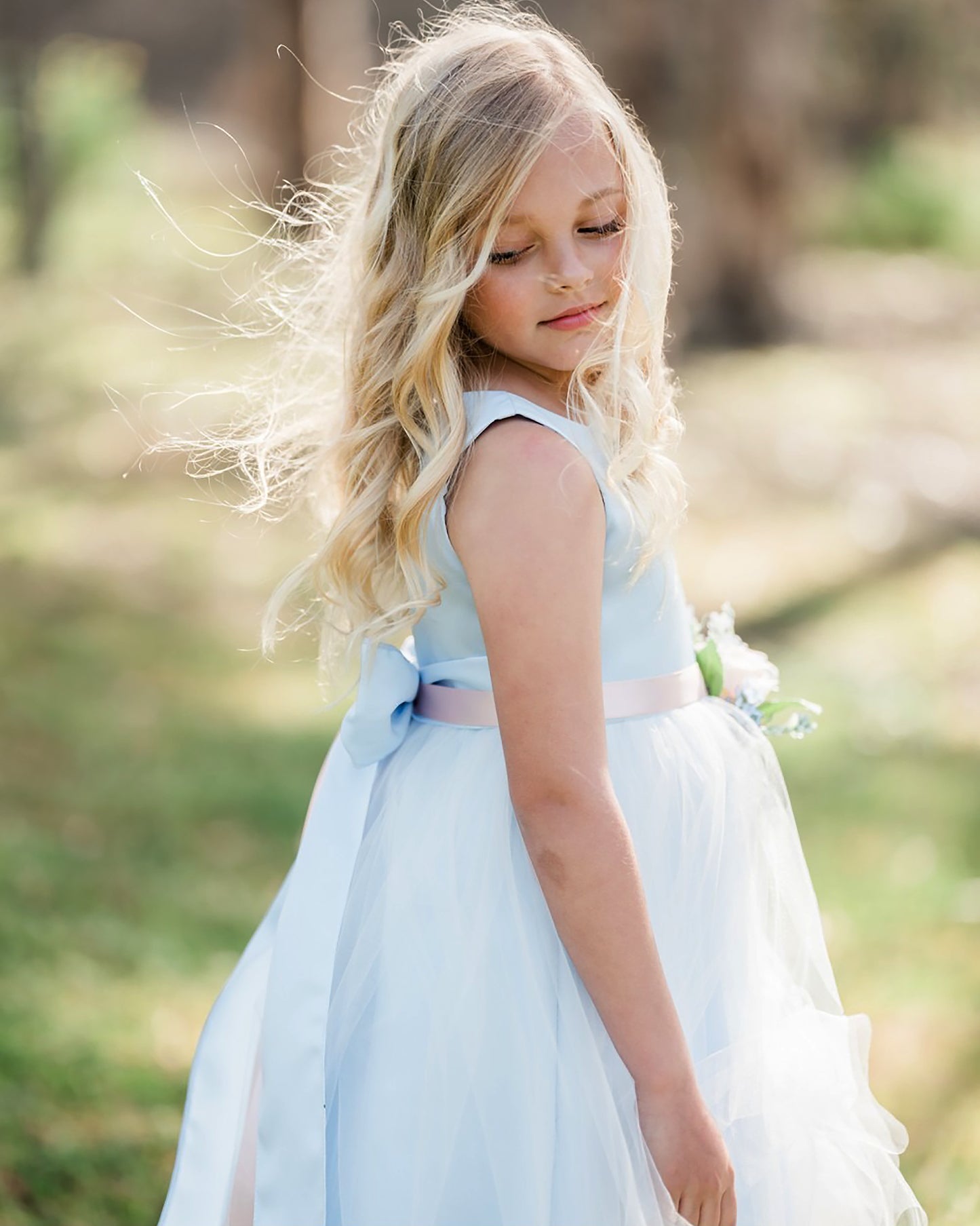 Young girl in a light blue dress standing outdoors with a blurred natural background