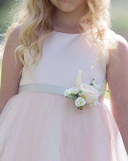 Young girl wearing a light pink dress with a floral corsage, standing outdoors.