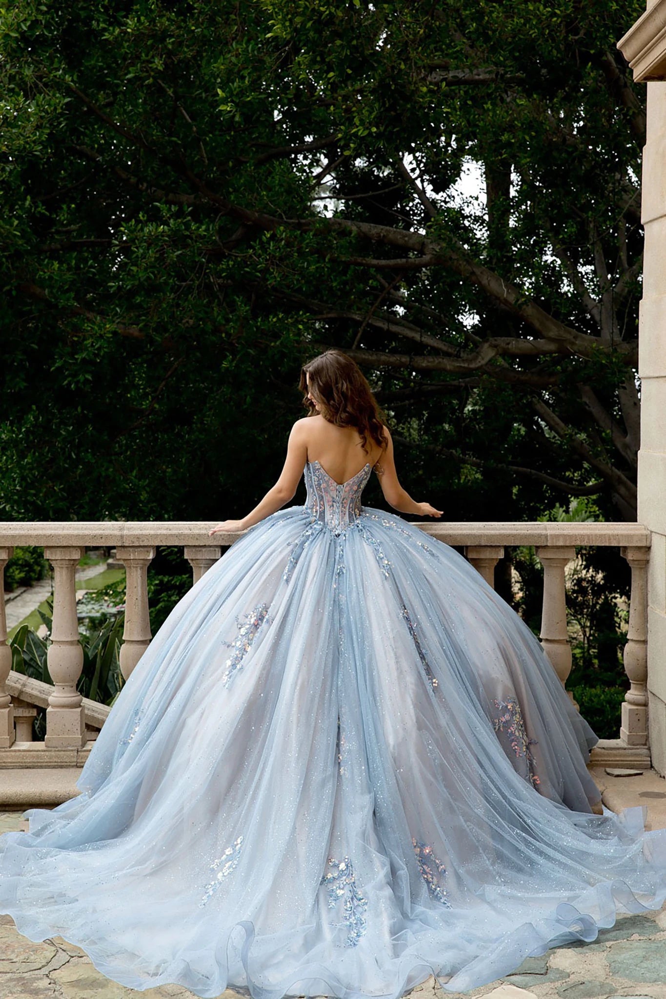 Woman in a light blue gown standing on a balcony with trees in the background