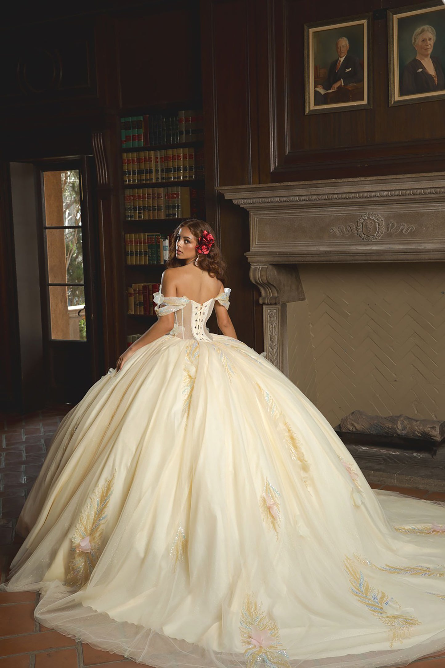 Woman in a white wedding dress with floral details in a room with bookshelves and portraits.