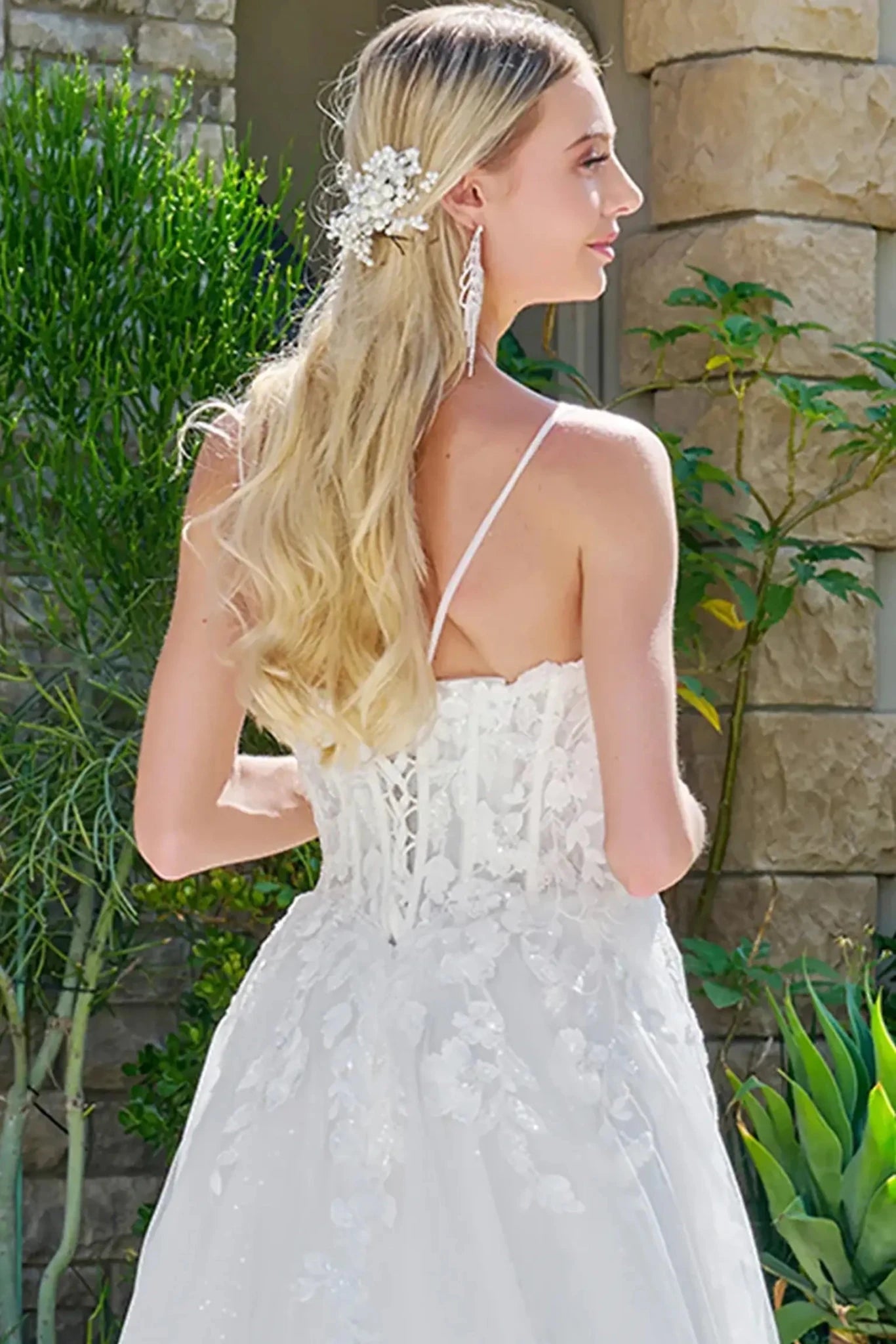Woman in a white lace dress with floral hairpiece standing outdoors.
