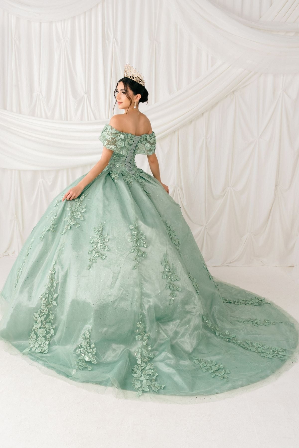 Side profile shows light Sage quinceanera ball gown with floral sequin appliques, glitter lace train, and layered skirt.