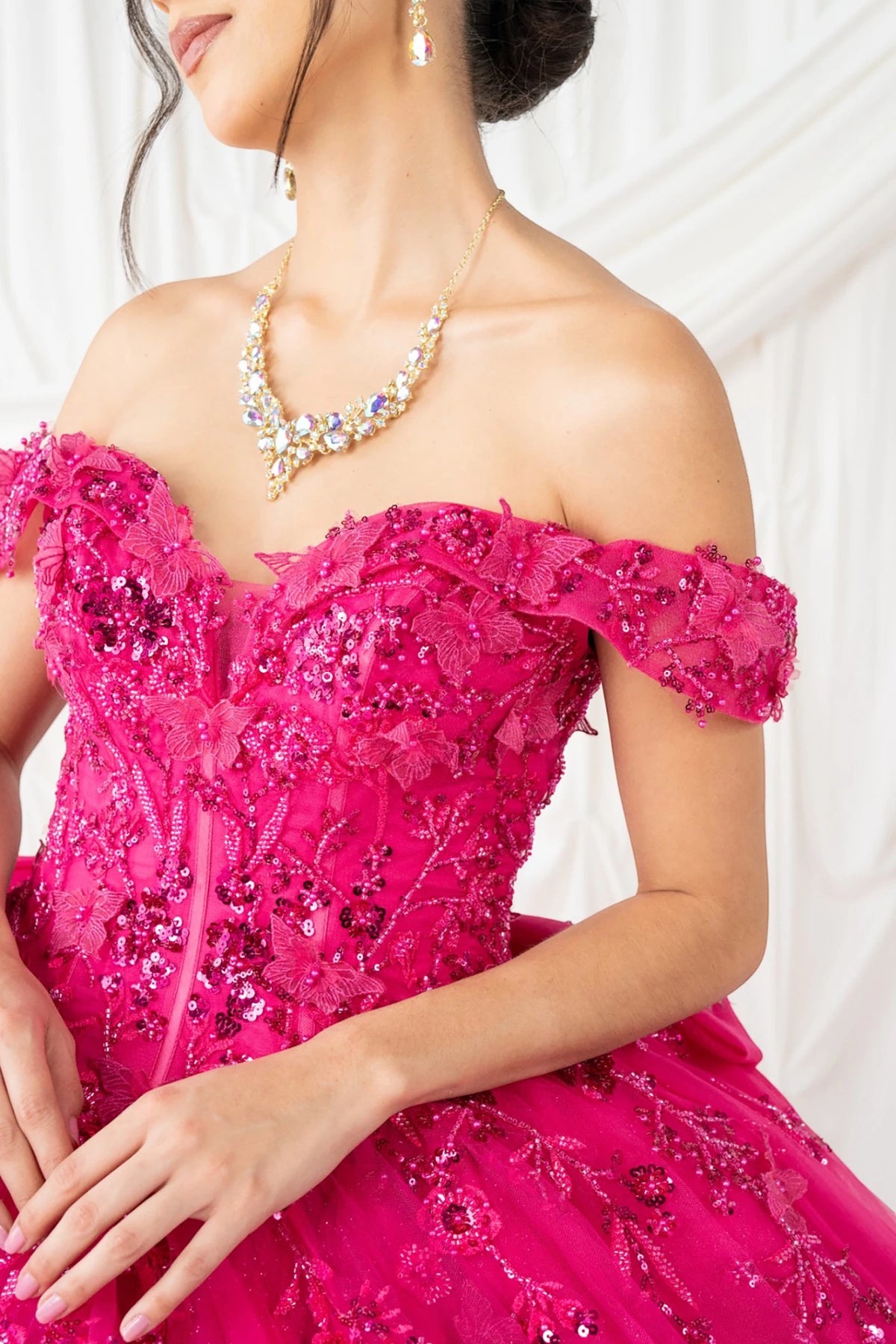 Bodice close-up highlights fuchsia quinceanera ball gown with off-shoulder neckline, butterfly appliques, rhinestones.