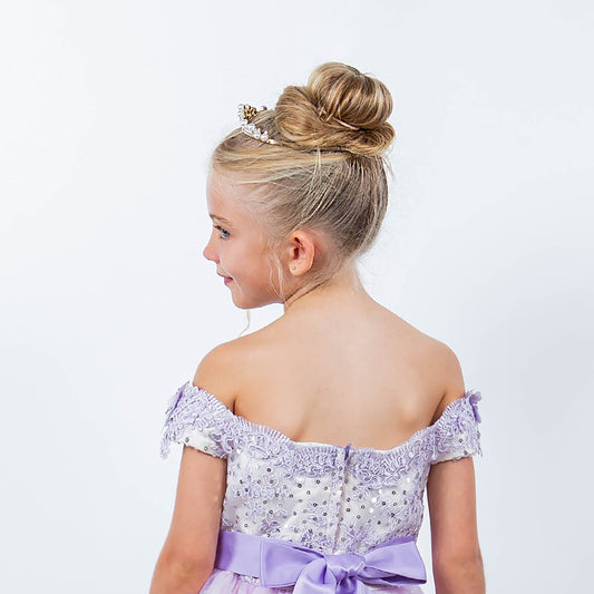 Young girl wearing a purple off-shoulder dress with a pearl tiara on a white background