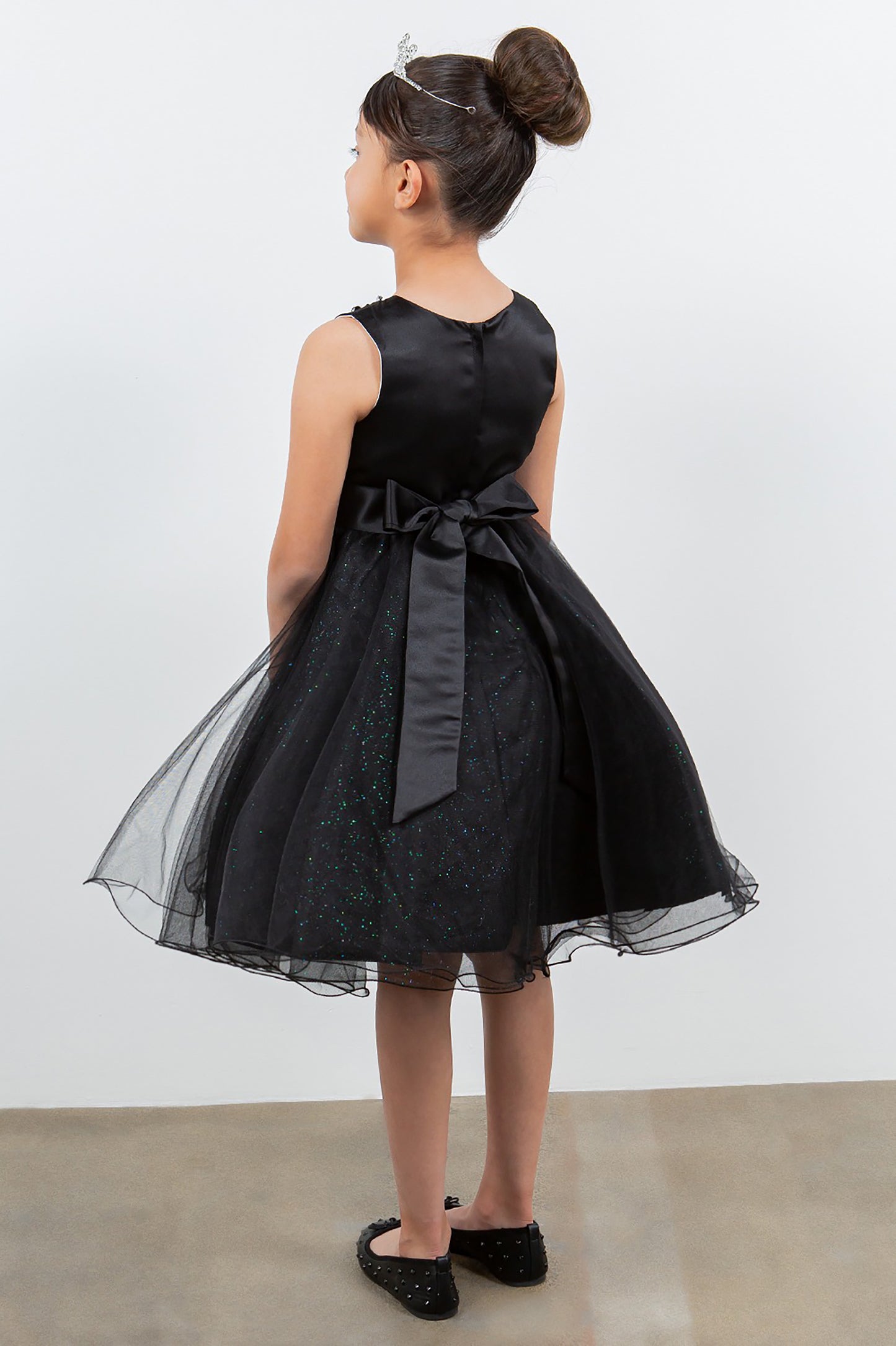 Young girl wearing a black dress with a bow, standing against a white background