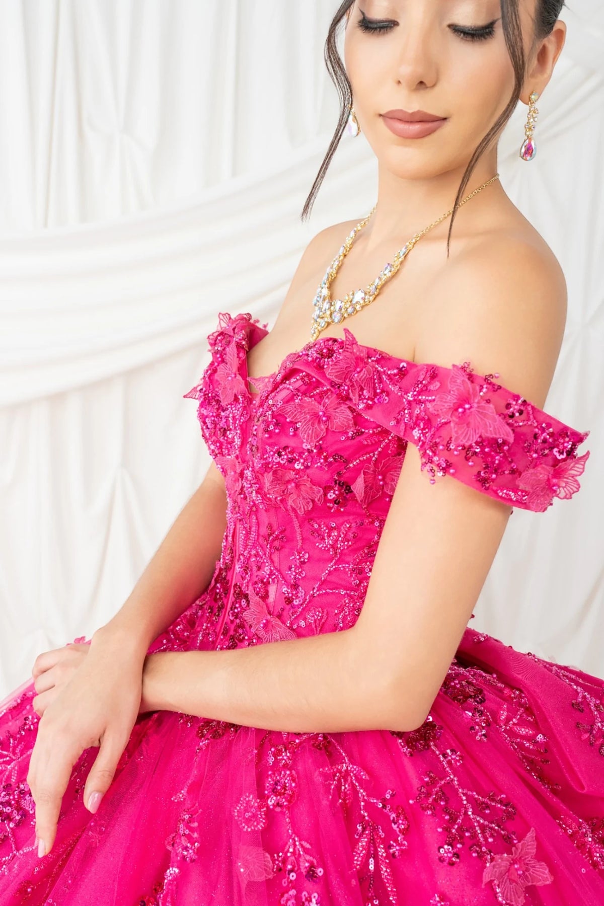 Side profile shows fuchsia quinceanera ball gown with butterfly appliques, rhinestone embellishments, and glitter tulle fabric.