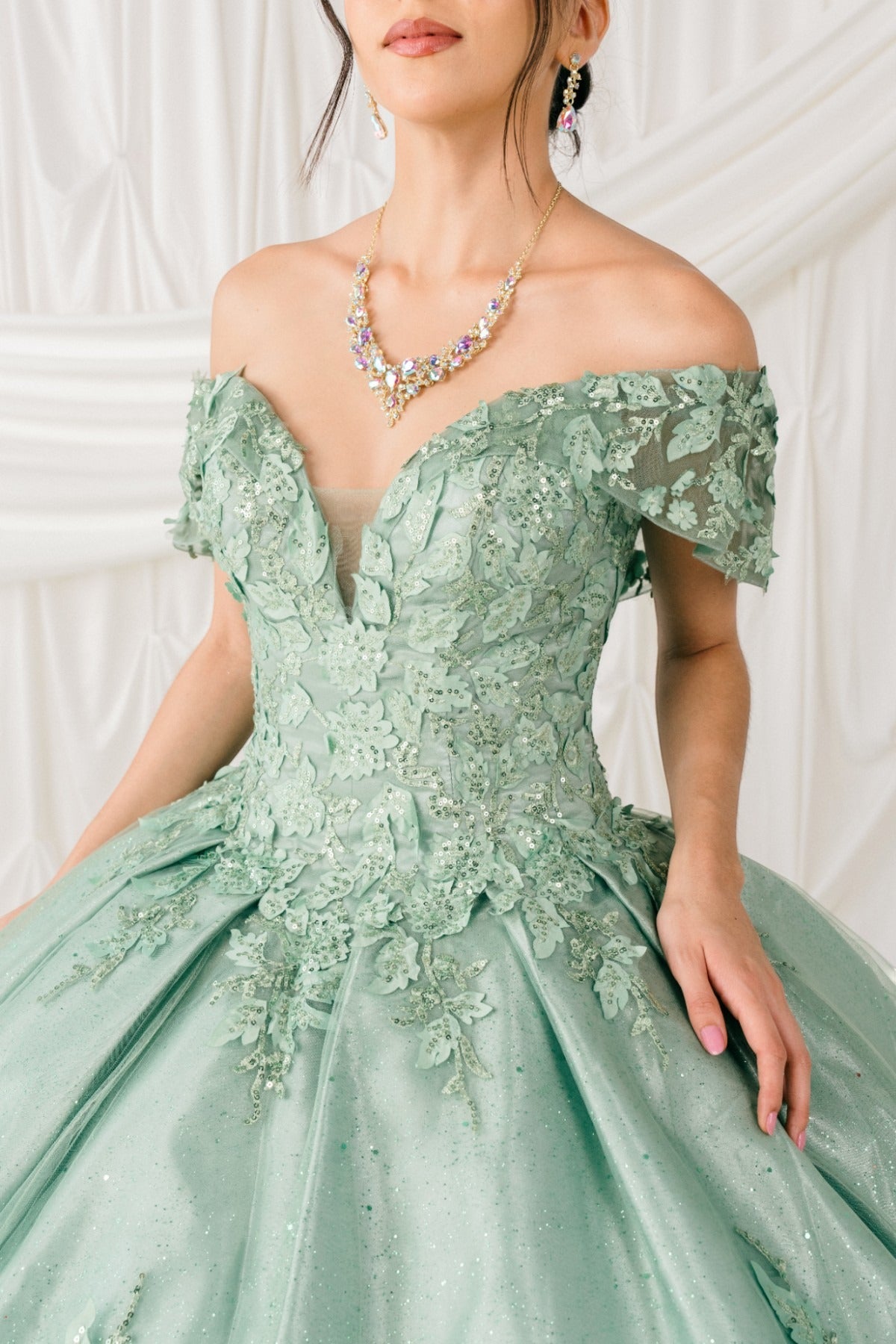 Skirt detail shows Sage quinceanera ball gown with off-shoulder lace appliques, glitter details, and layered skirt.
