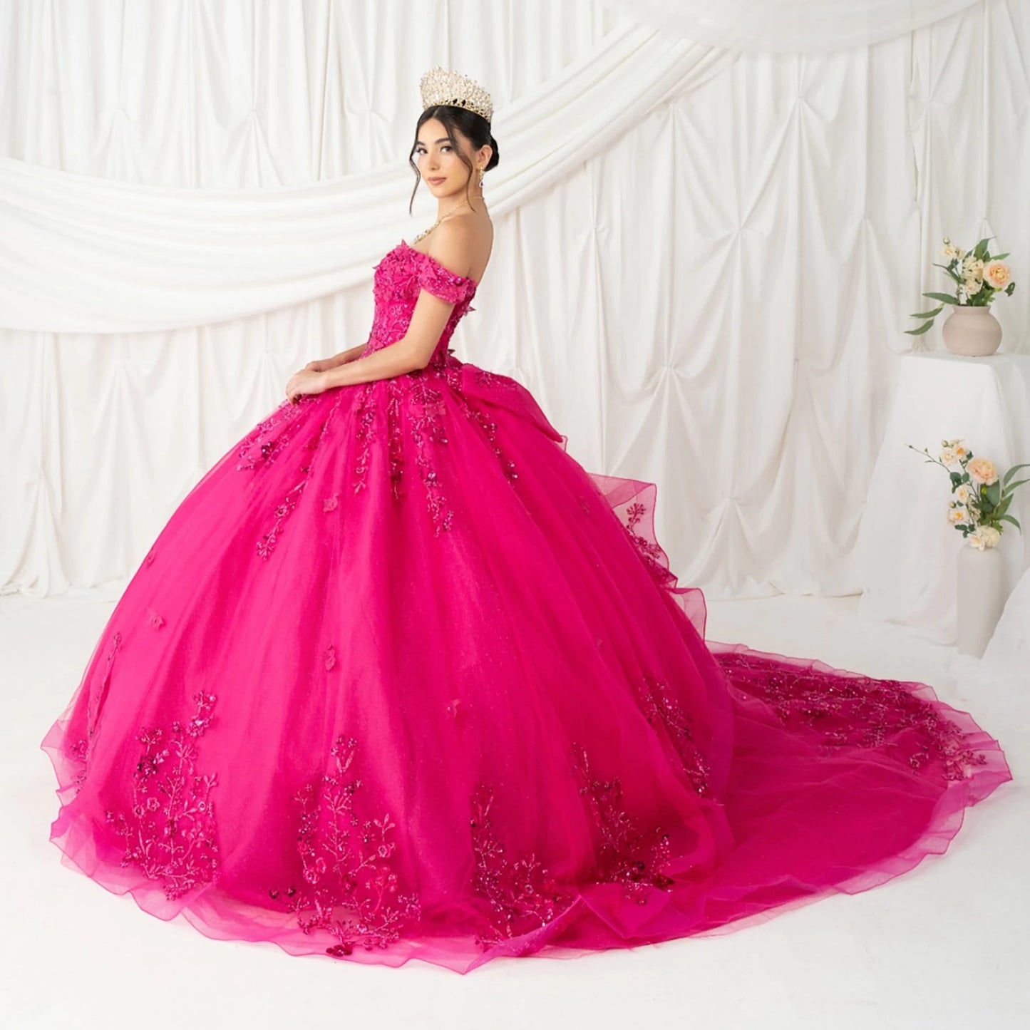 Front view of a woman wearing fuchsia quinceanera ball gown with butterfly appliques, rhinestone accents, and glitter tulle skirt