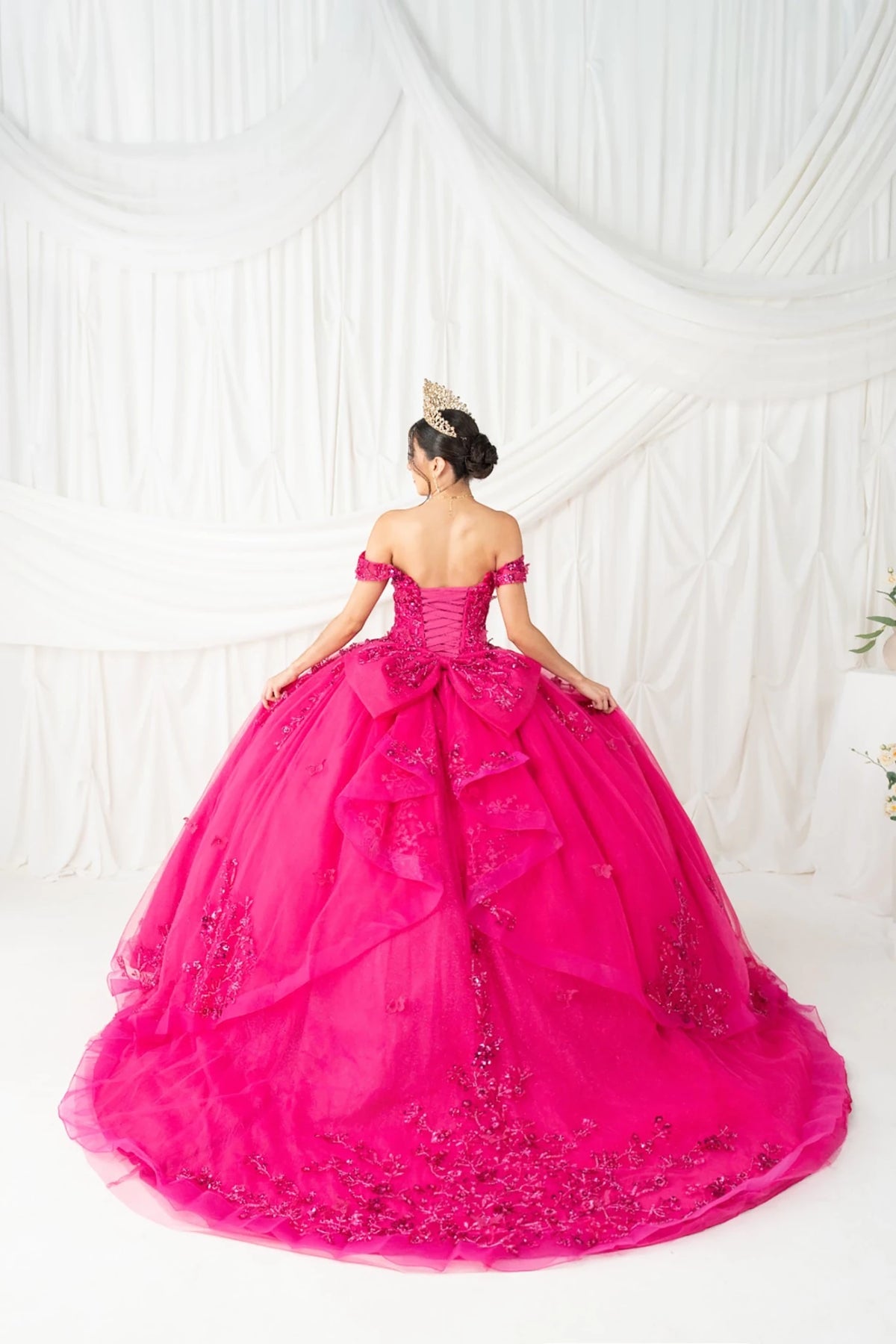 Rear view reveals fuchsia quinceanera ball gown with butterfly appliques, rhinestone detailing, and layered skirt.