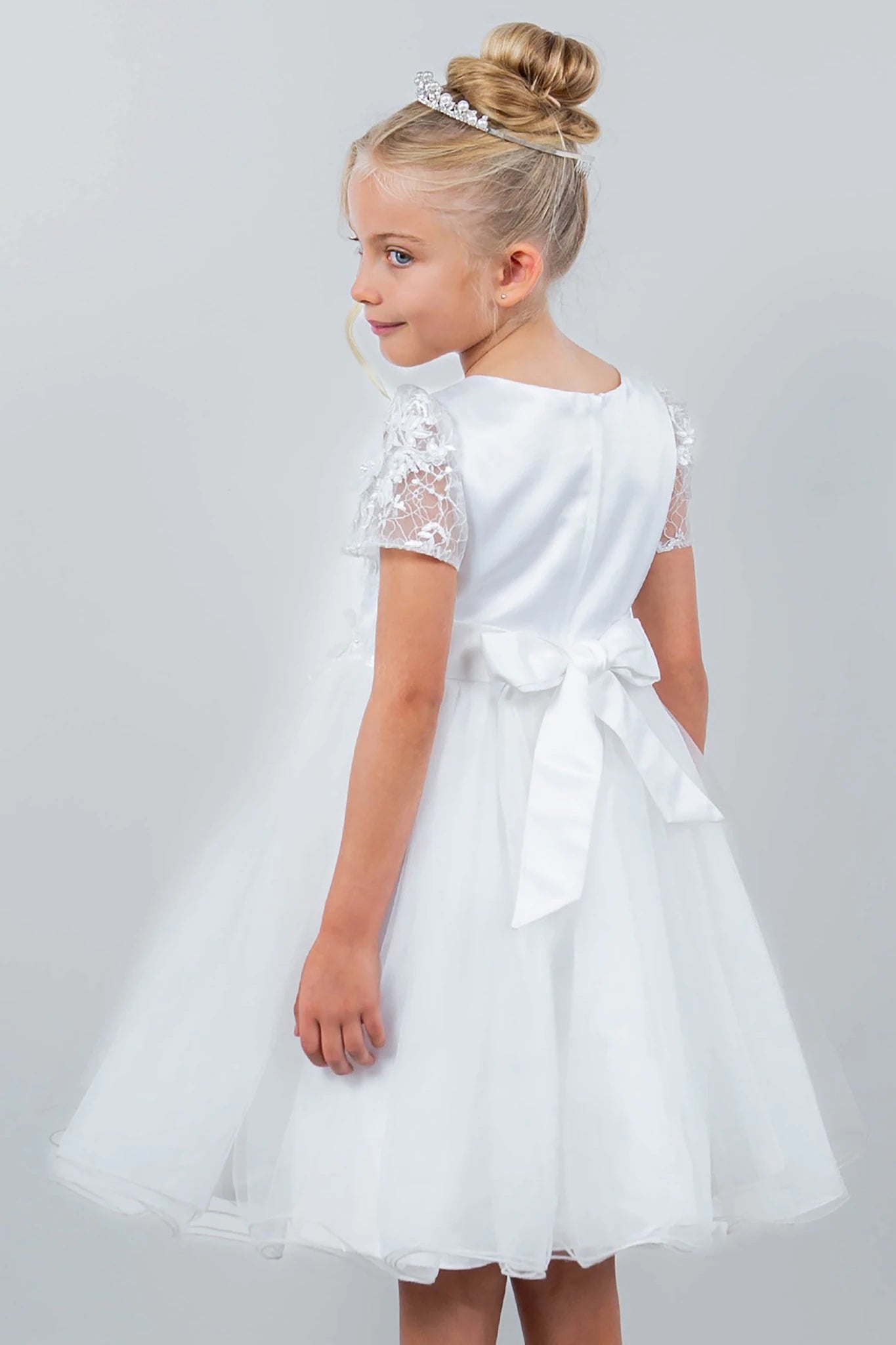 Young girl wearing a white dress with lace sleeves on a plain background
