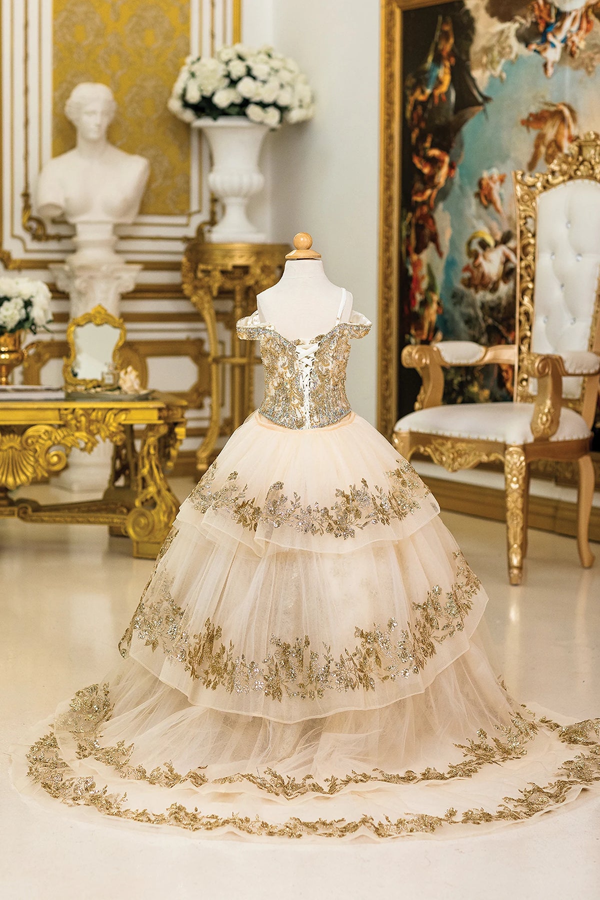From behind, the Champagne mini quinceañera dress features tiered detachable train extending from the embroidered back.
