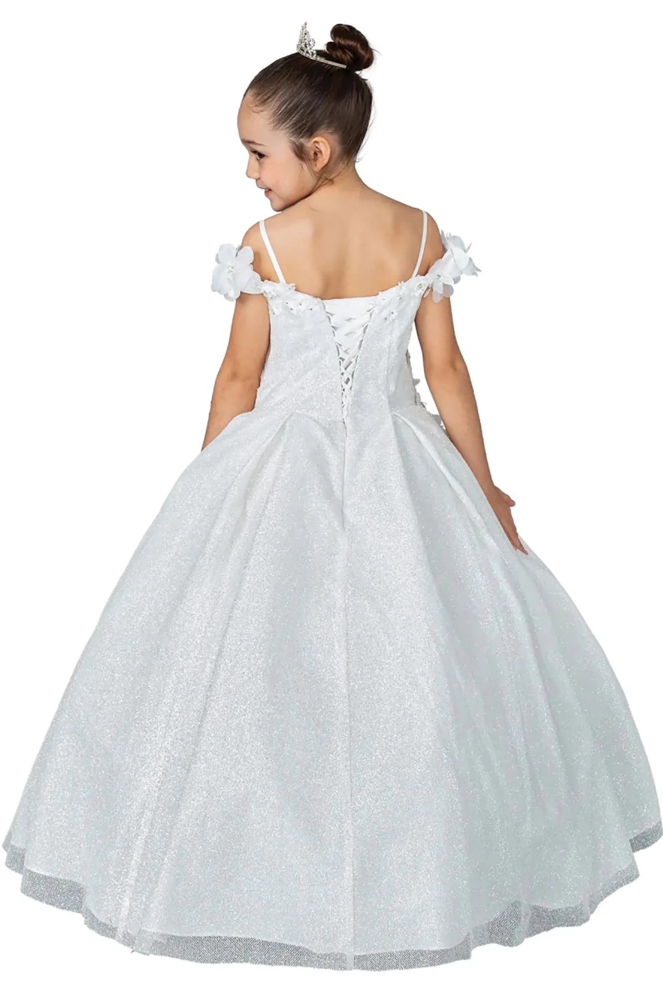 Young girl standing back-facing in white kids mini quinceañera dress with lace-up bodice, floral shoulder appliqués, and glitter tulle skirt