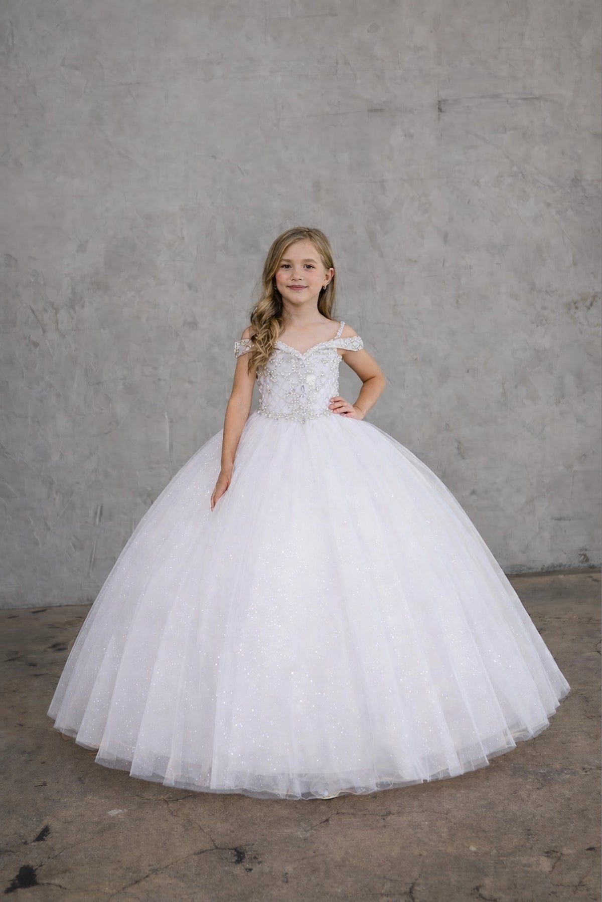 A closer look shows, the White/Silver mini quince dress showcases metallic embroidered off-the-shoulder bodice and full tulle skirt with coordinating two-tone detail.