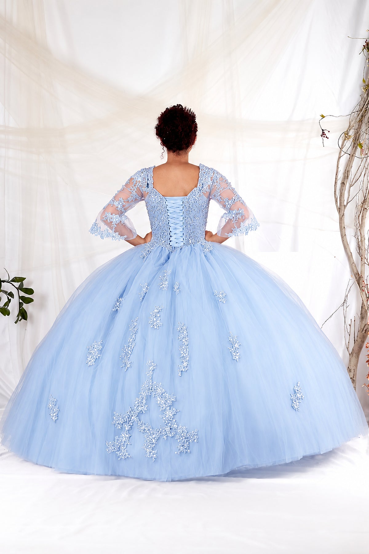 Bahama Blue quinceañera ball gown shown from the back with lace-up detailing, embroidered sheer sleeves and a full skirt.