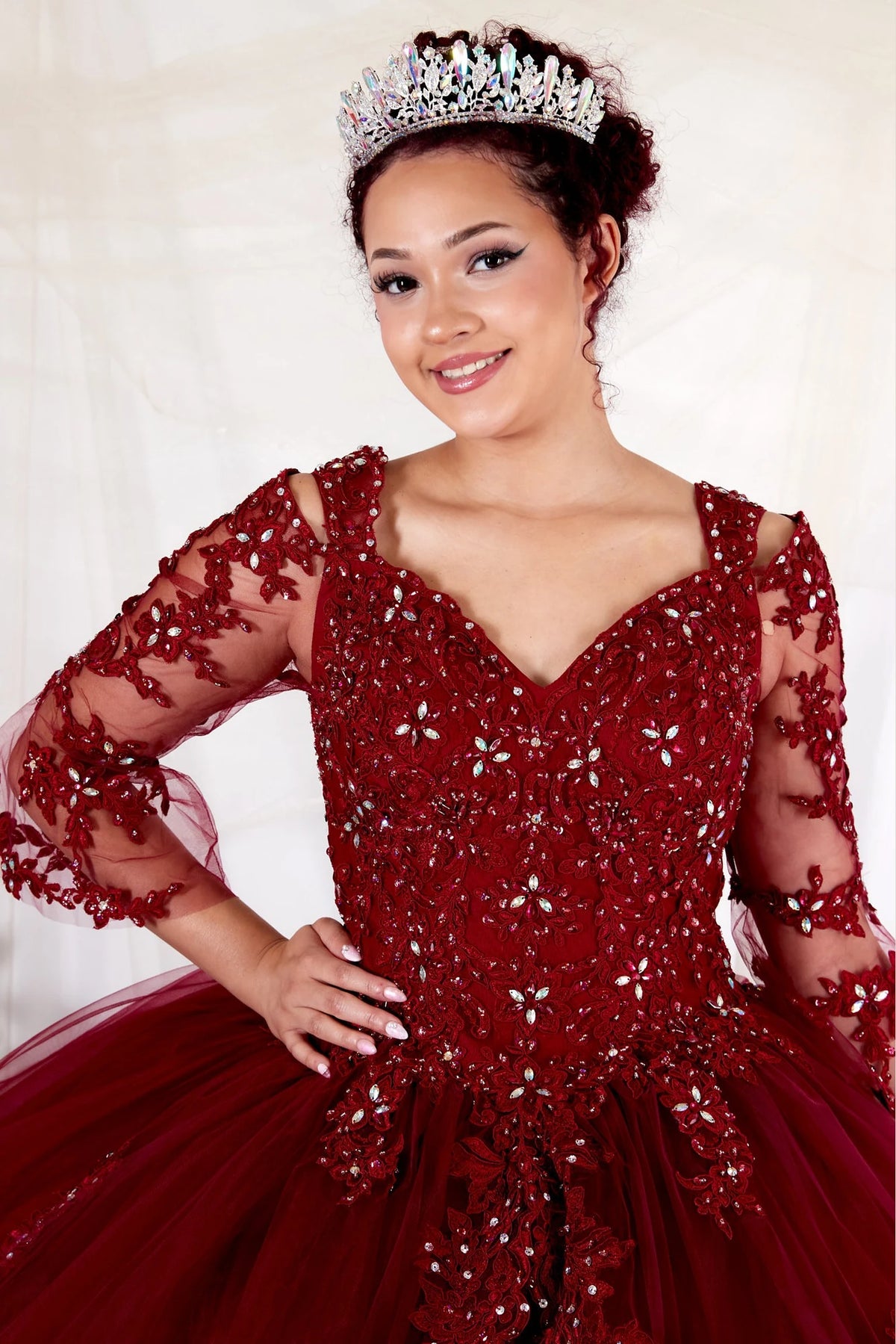 A V-shaped neckline and sheer floral sleeves frame the embellished bodice of the Burgundy quinceañera ball gown.