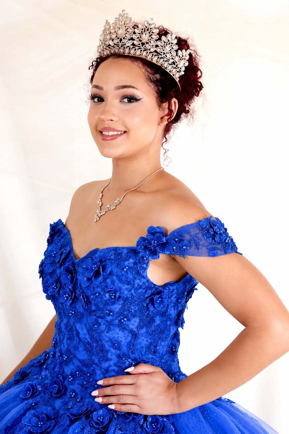 Dimensional floral appliqués and glitter accents defines the Royal Blue quinceañera dress in this detailed view.