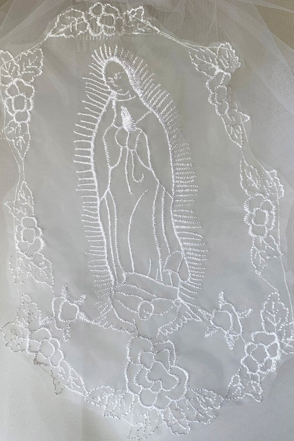 Textured details appear across white lace Virgin Mary embroidered first communion lace applique.