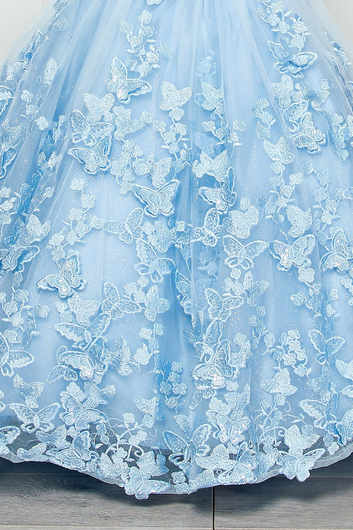 Skirt detail of a blue kids mini quinceanera mini quince dress with layered glitter tulle fabric, butterfly floral appliques, and detachable cape.