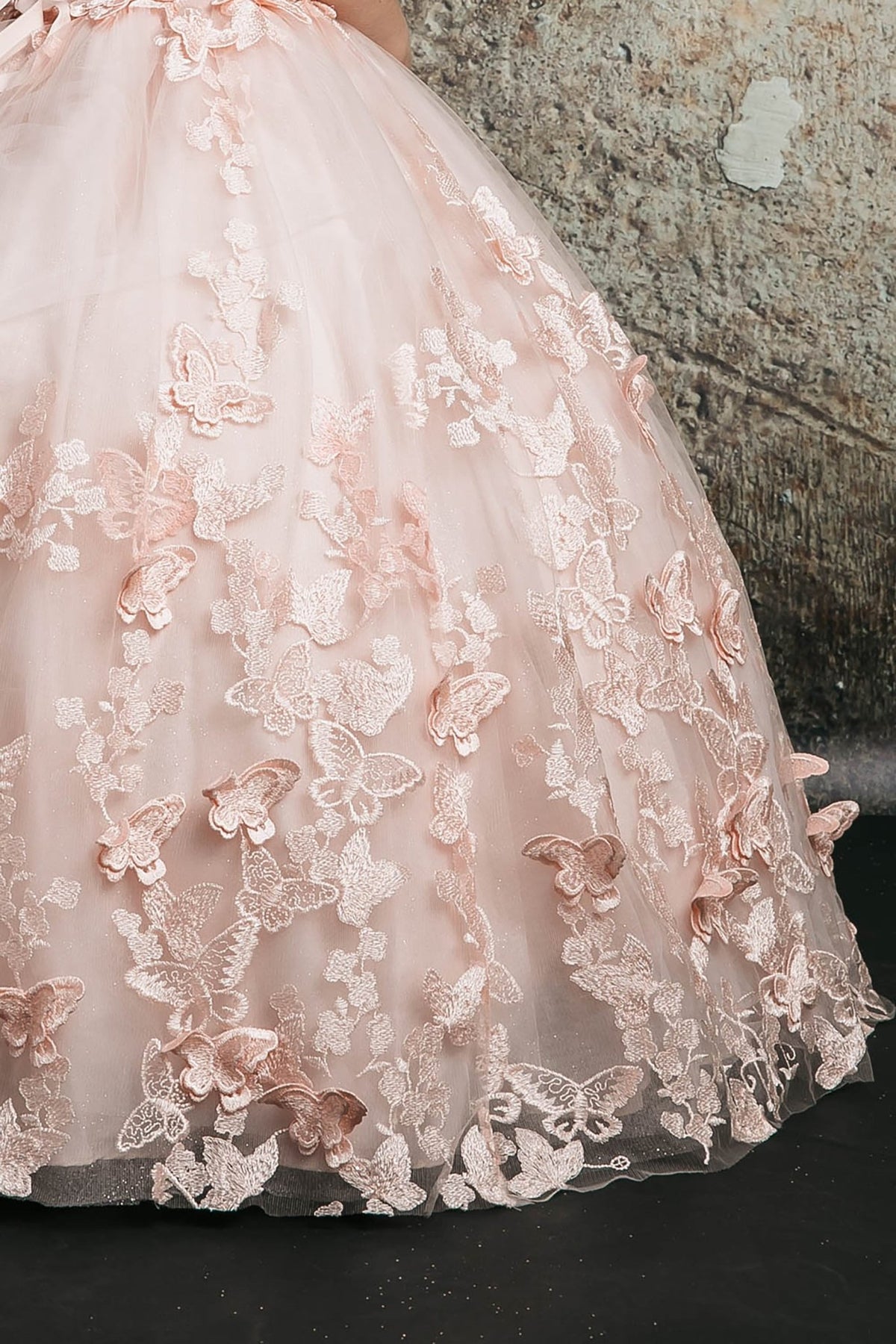 Skirt detail of a blush kids mini quinceanera mini quince dress with layered glitter tulle fabric, butterfly floral appliques, and detachable cape.