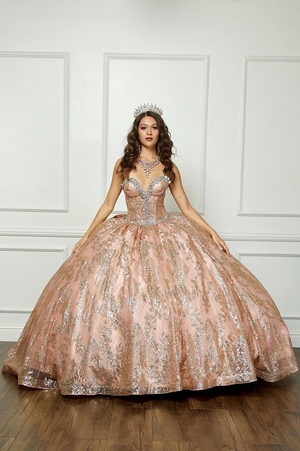 Front view of a woman wearing a gold quinceañera ball gown with sparkling sequin embellishments, corset bodice and tulle skirt