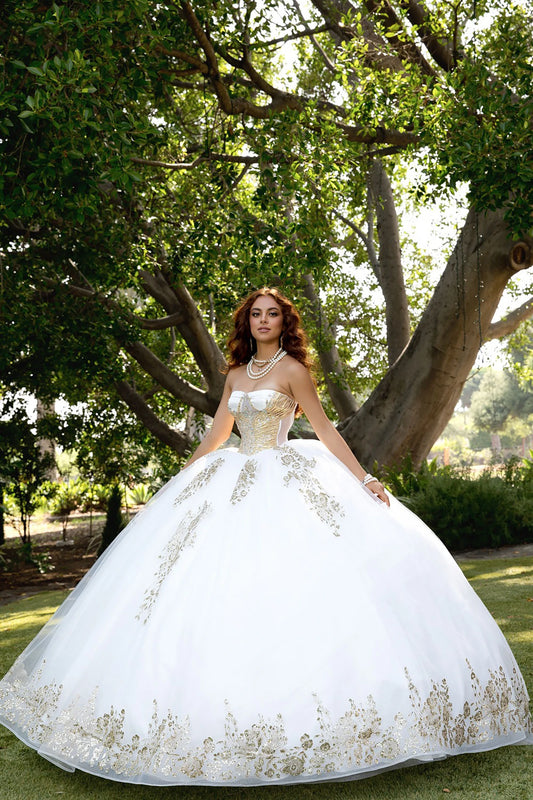 Woman in a white and gold embroidery ball gown dress standing in a park with trees and grass.