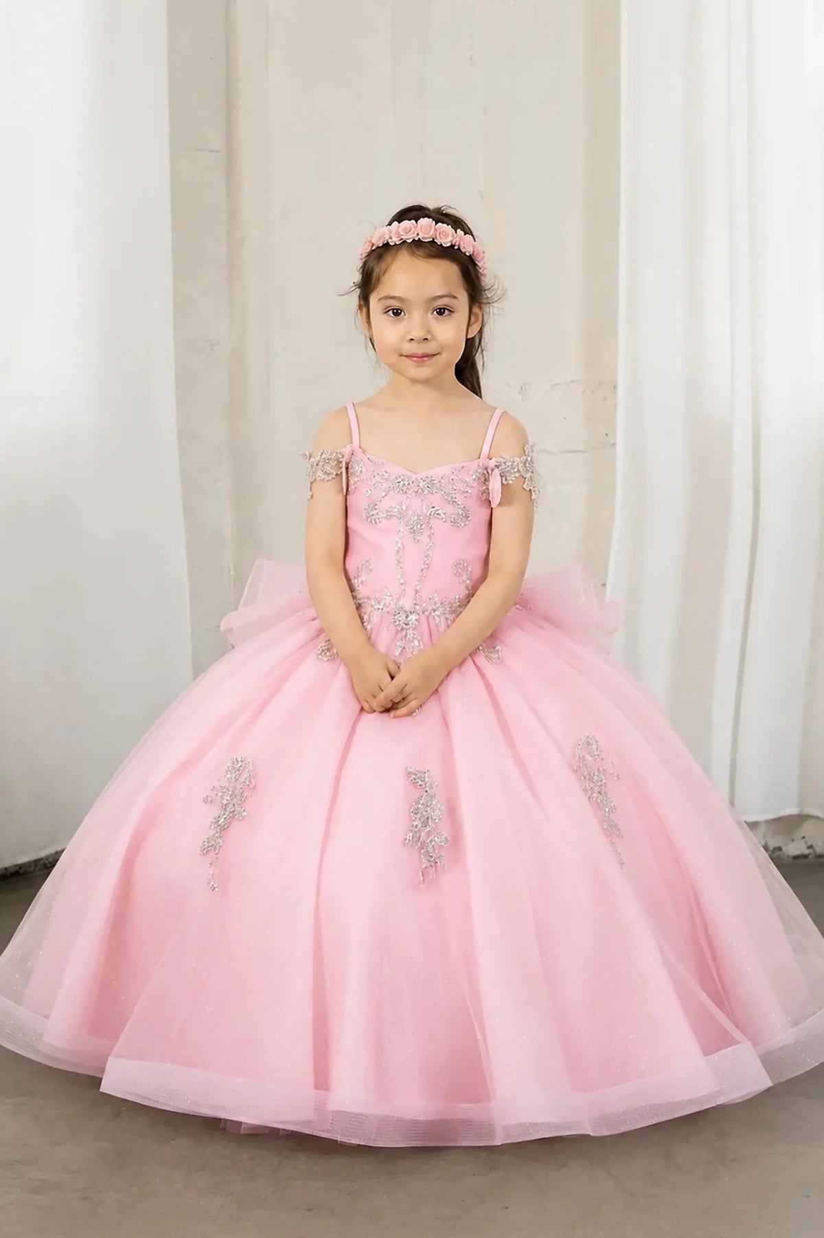 A young girl wearing a pink off-the-shoulder ball gown with silver sequin embroidery