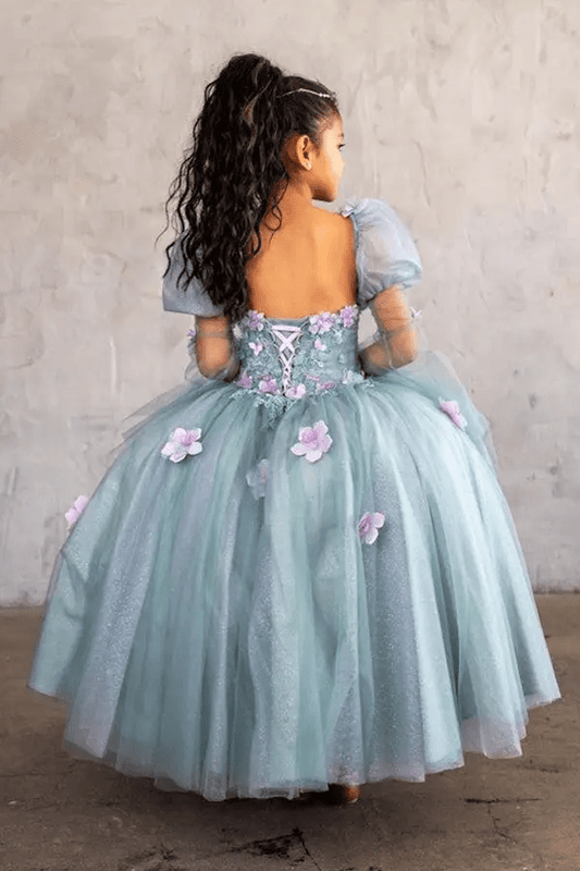Kid standing back-facing in sage ball gown with lace-up closure, 3D flower detailing, removable sleeves, and cascading skirt