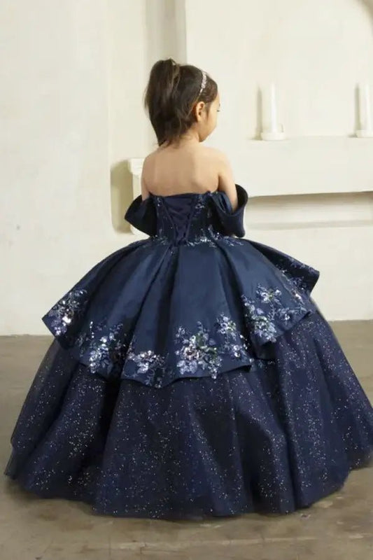 Kid standing back-facing in navy ball gown with lace-up corset closure, glitter tulle layers, and cascading full skirt