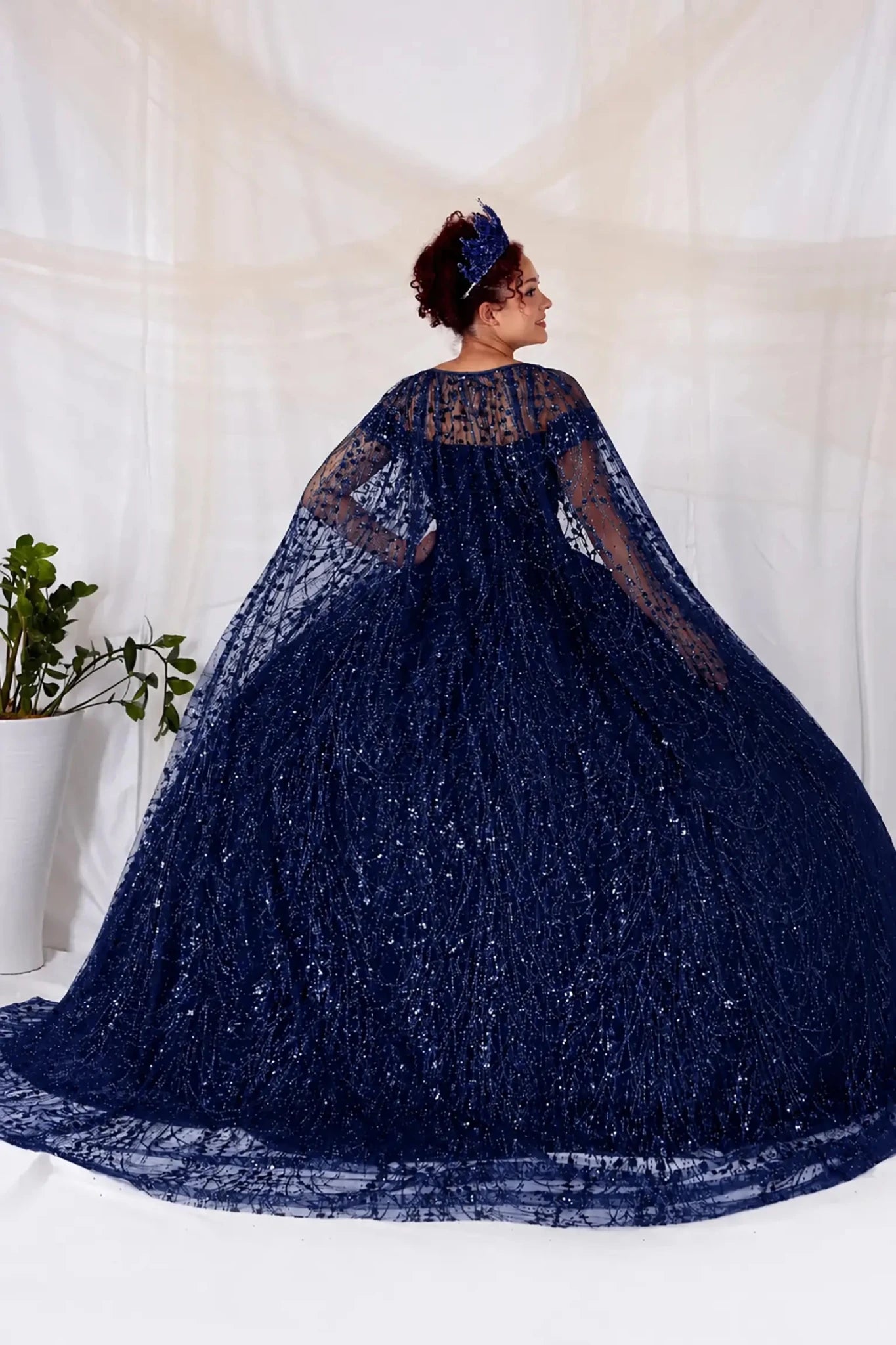 Person wearing a navy blue embroidered quinceanera dress with a cape