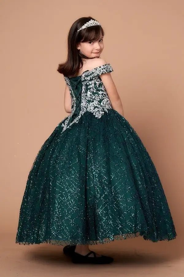 Kid standing side-facing in emerald green ball gown with dimensional 3D floral detail, shimmering glitter tulle highlights, and flowing layered skirt