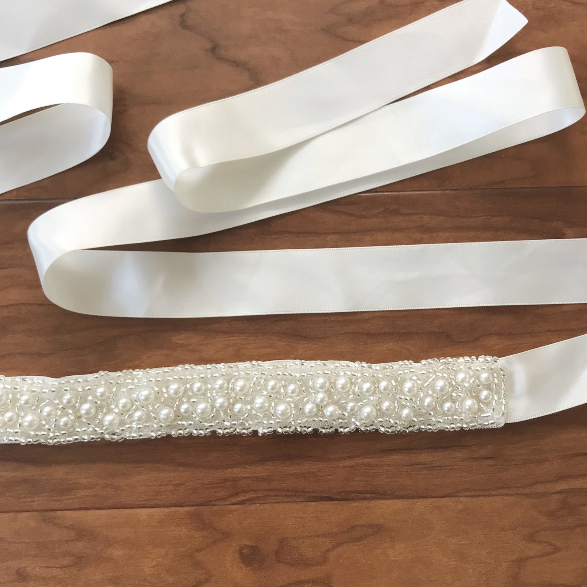 Ivory satin ribbon with a beaded and pearl embellished belt on a wooden surface