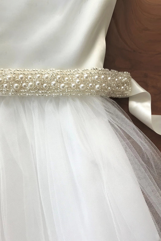 Close-up of a ivory dress with a pearl belt on a wooden surface