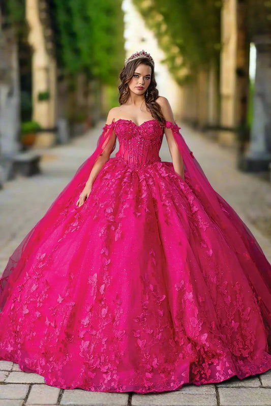 Woman standing front-facing in fuchsia quinceañera ball gown with dramatic off-shoulder design, beaded bodice, intricate floral embroidery, full tulle skirt, and elegant cape details