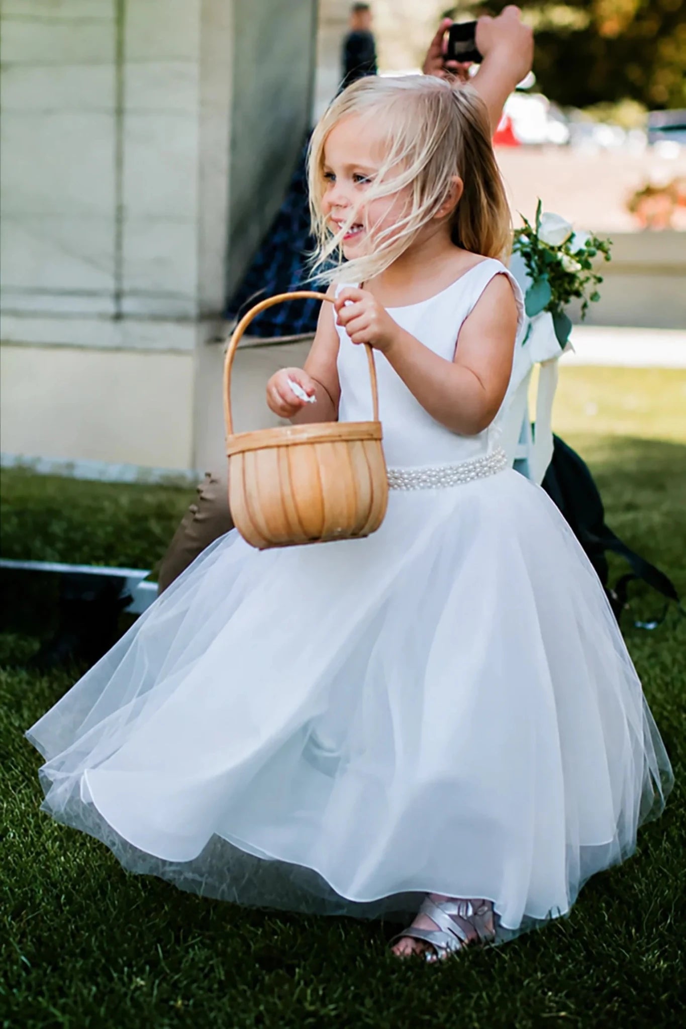 A young girl in a sleeveless white tulle dress with pearl sash