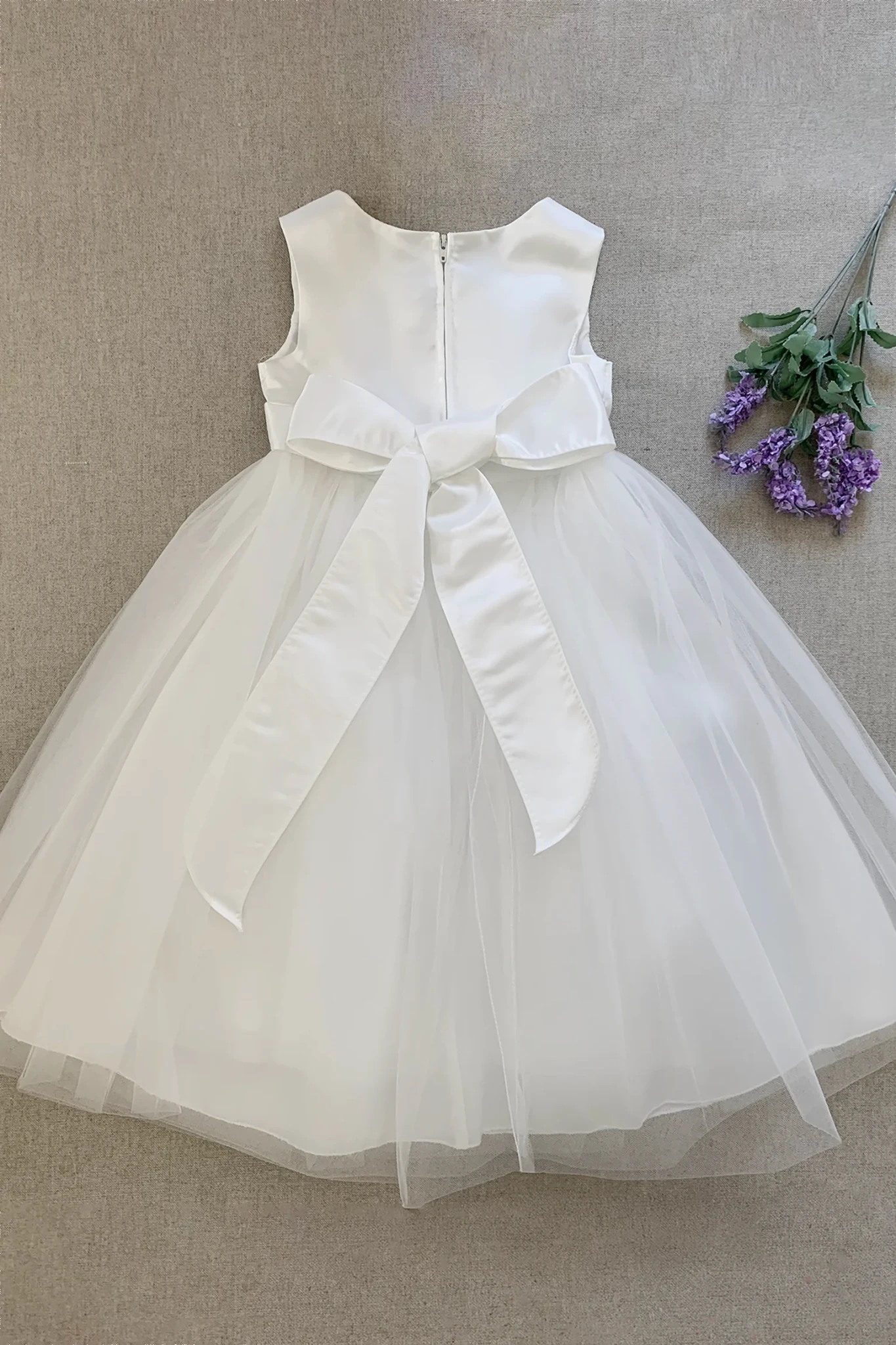 A sleeveless white kids tulle dress with a large satin bow at the waist